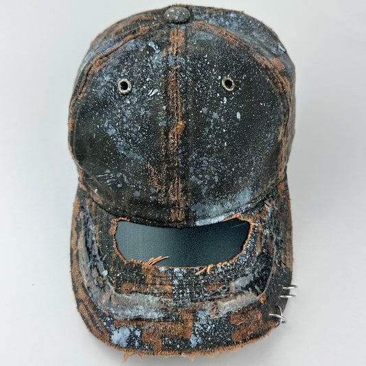 Cover image of ASTROBOI* brown distressed leather hat with white paint splatter, stainless steel piercings on visor and glossy clear resin finish.