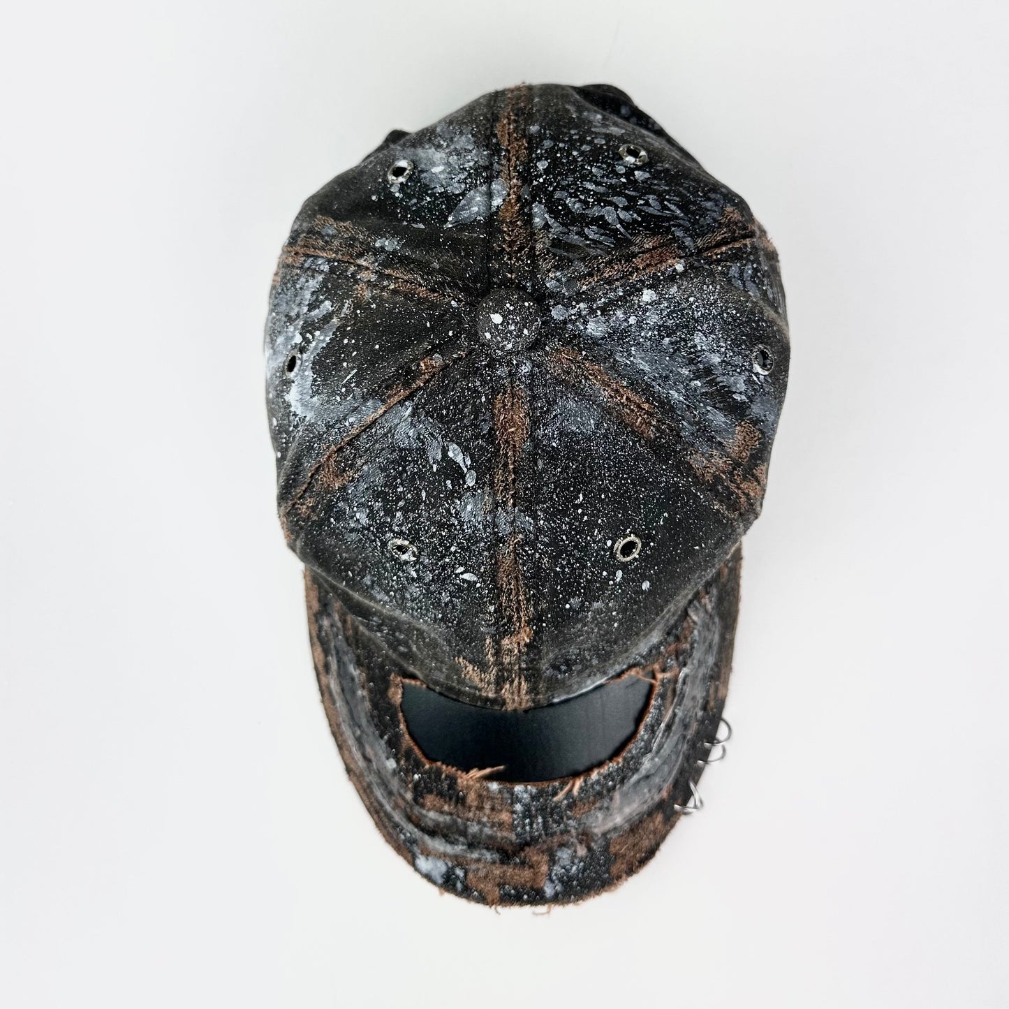 Top of ASTROBOI* brown distressed leather hat with white paint splatter, stainless steel piercings on visor and glossy clear resin finish.