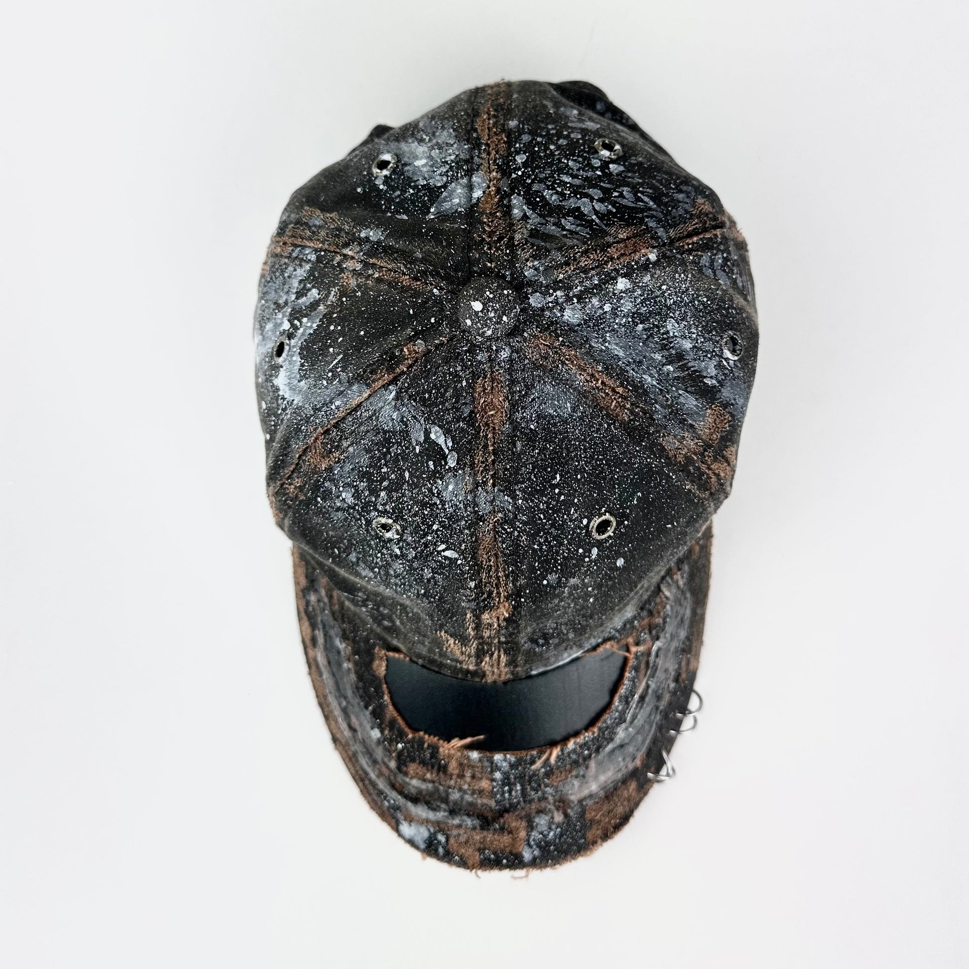 Top of ASTROBOI* brown distressed leather hat with white paint splatter, stainless steel piercings on visor and glossy clear resin finish.