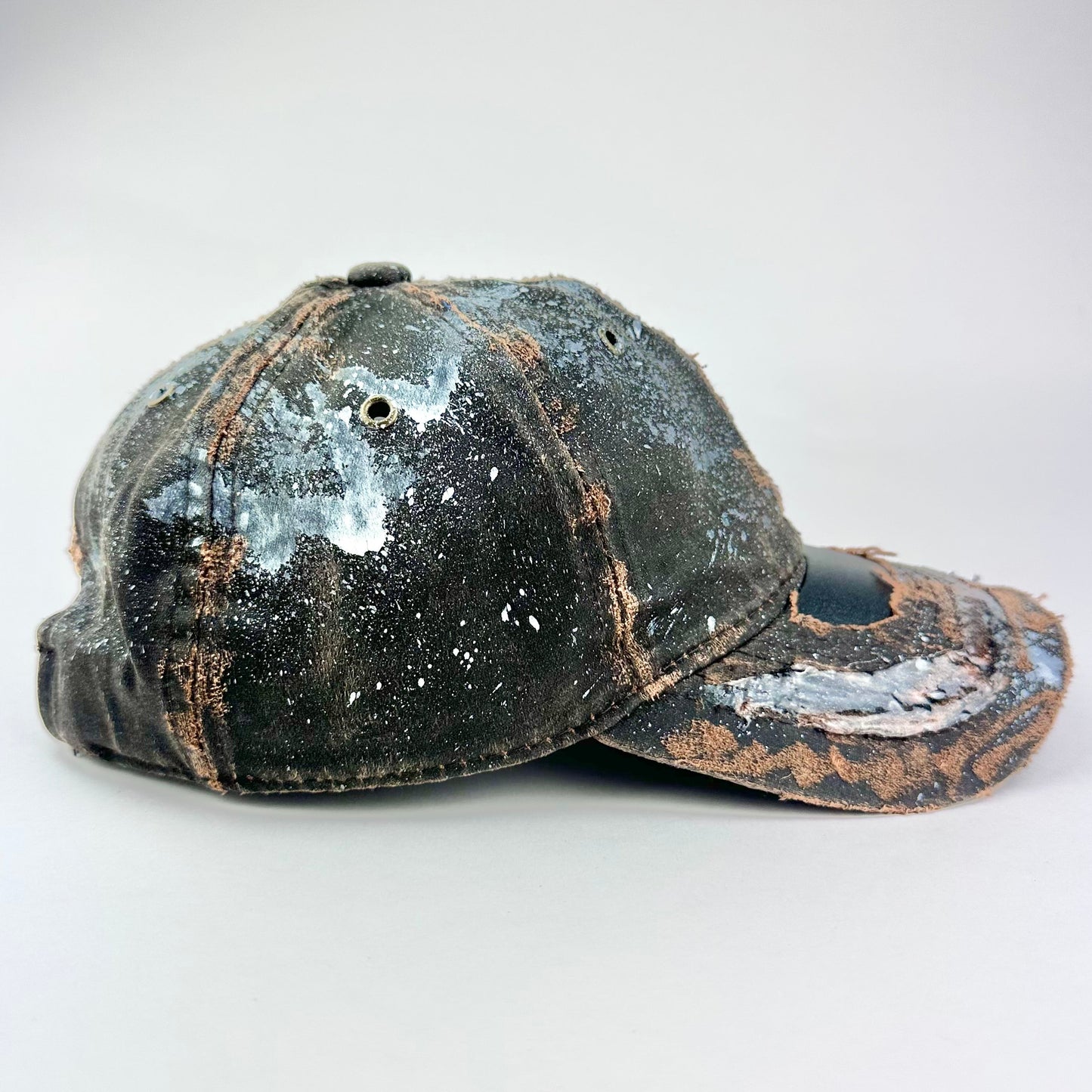 Right side of ASTROBOI* brown distressed leather hat with white paint splatter, stainless steel piercings on visor and glossy clear resin finish.
