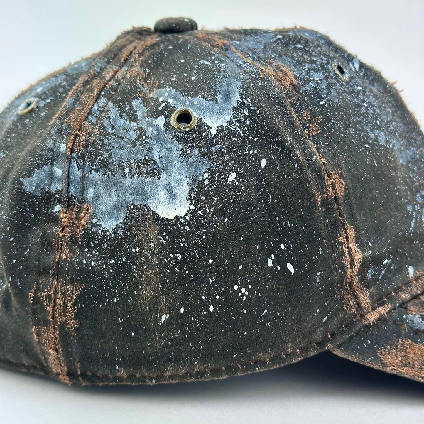 Paint splatter detail on ASTROBOI* brown distressed leather hat with white paint splatter, stainless steel piercings on visor and glossy clear resin finish.