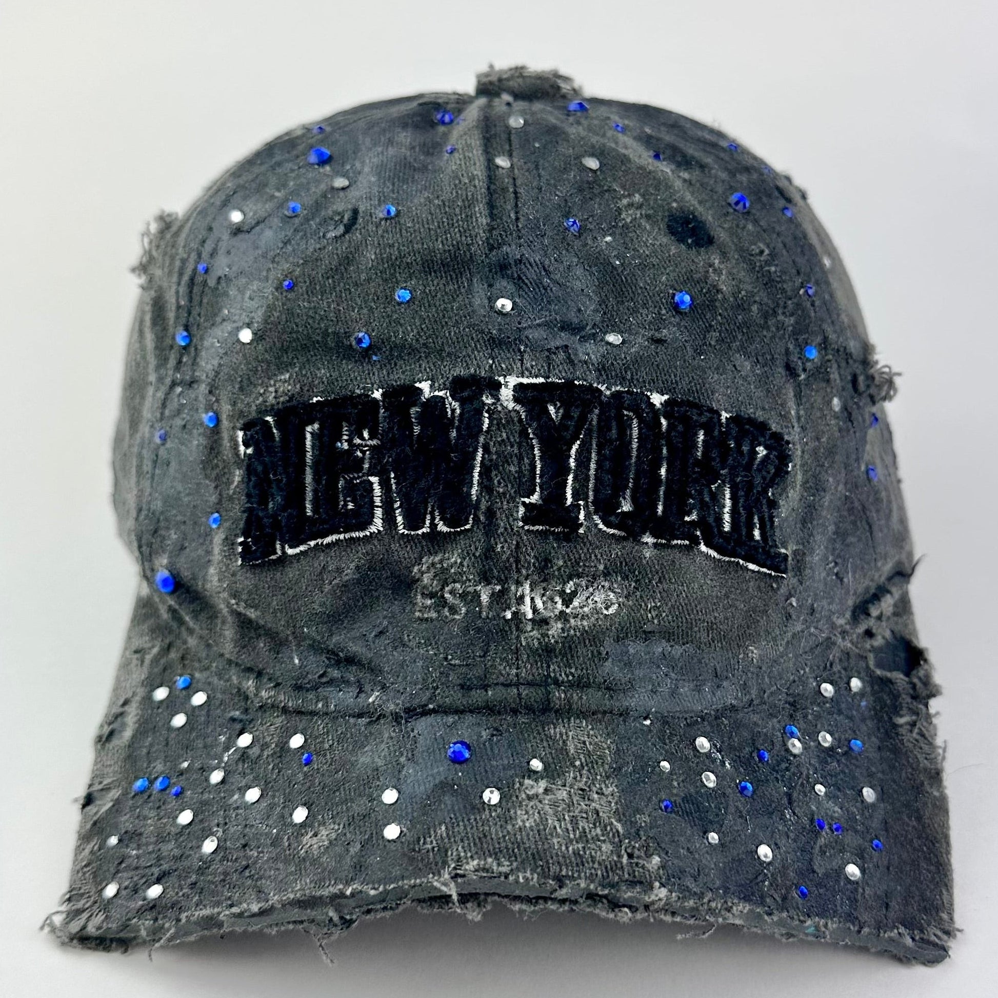 Front of ASTROBOI* 'Oceane' black distressed half visor hat featuring New York logo, rhinestone accents, black metallic paint, and raw hem edge.