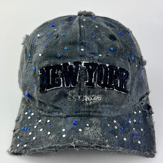 Front of ASTROBOI* 'Oceane' black distressed half visor hat featuring New York logo, rhinestone accents, black metallic paint, and raw hem edge.