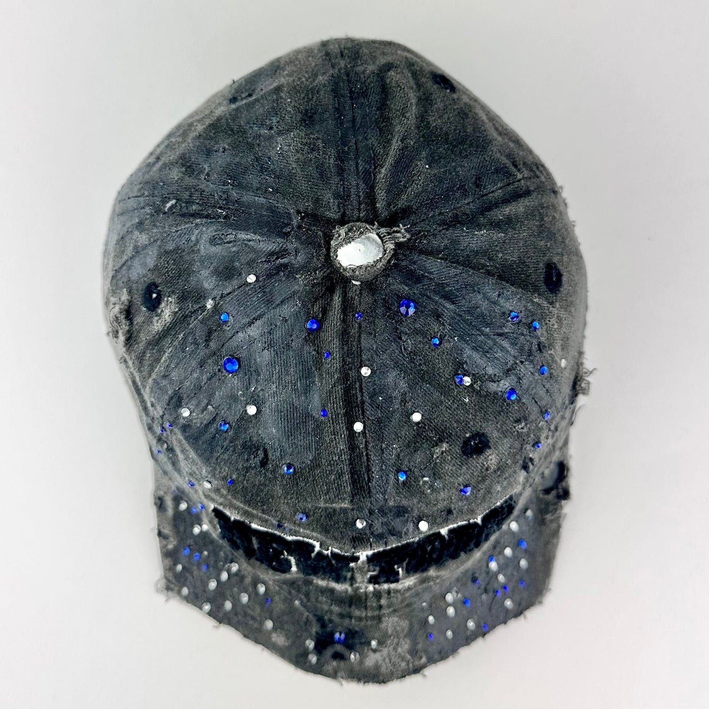 Top of ASTROBOI* 'Oceane' black distressed half visor hat featuring New York logo, rhinestone accents, black metallic paint, and raw hem edge.