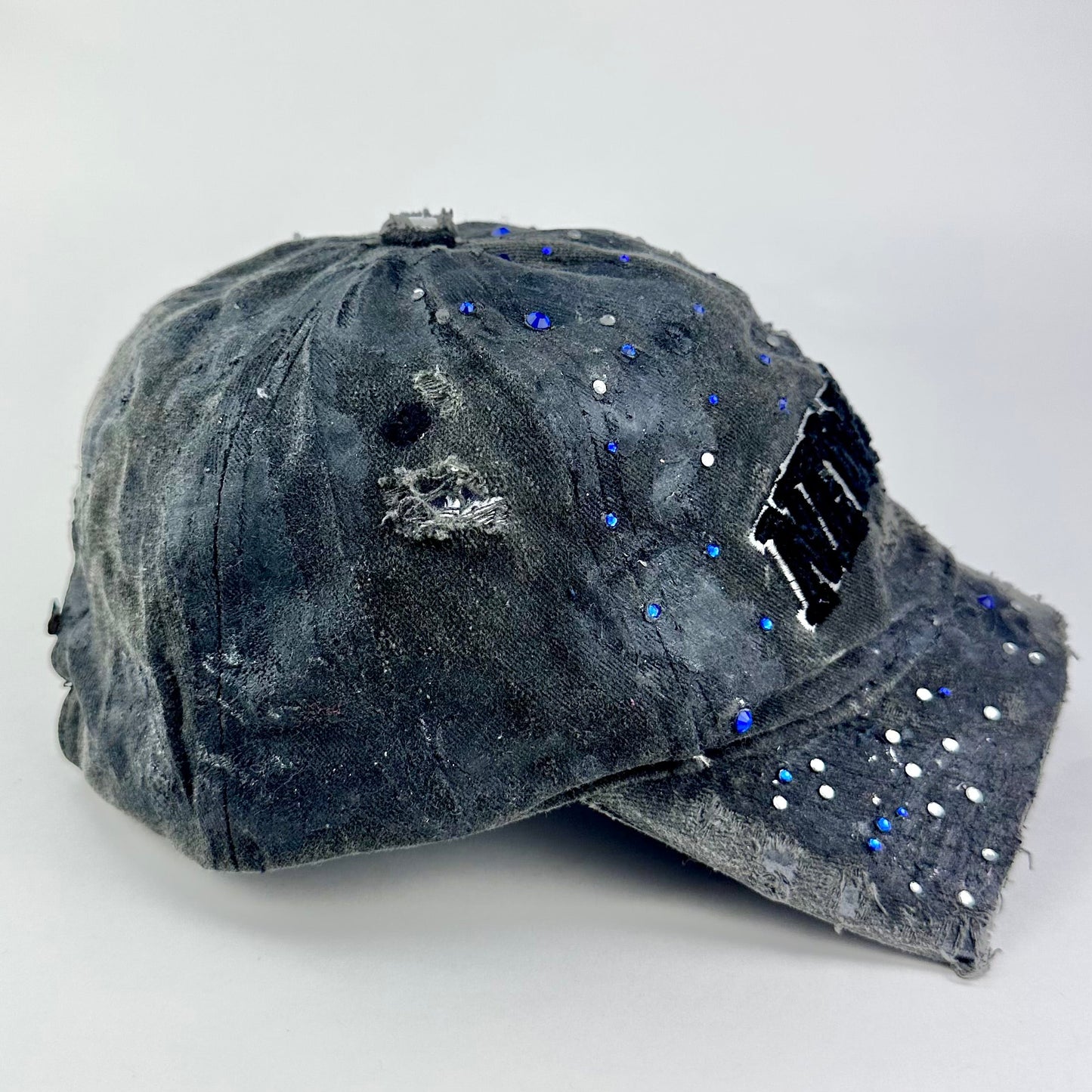 Right side of ASTROBOI* 'Oceane' black distressed half visor hat featuring New York logo, rhinestone accents, black metallic paint, and raw hem edge.