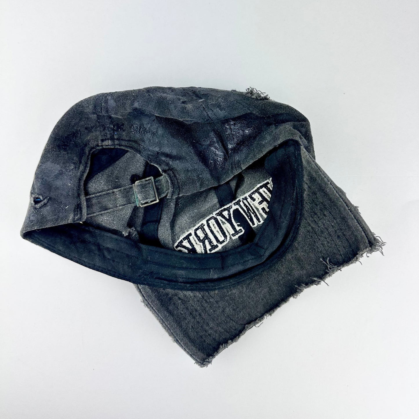 Back of ASTROBOI* 'Oceane' black distressed half visor hat featuring New York logo, rhinestone accents, black metallic paint, and raw hem edge.