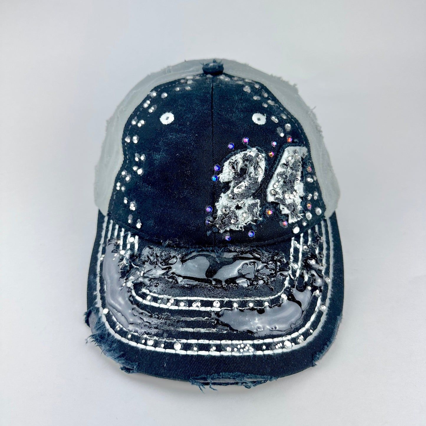 Front of ASTROBOI* “24” black racing cap with silver rhinestones, white stitching, glossy black resin details, and adjustable Velcro back closure.