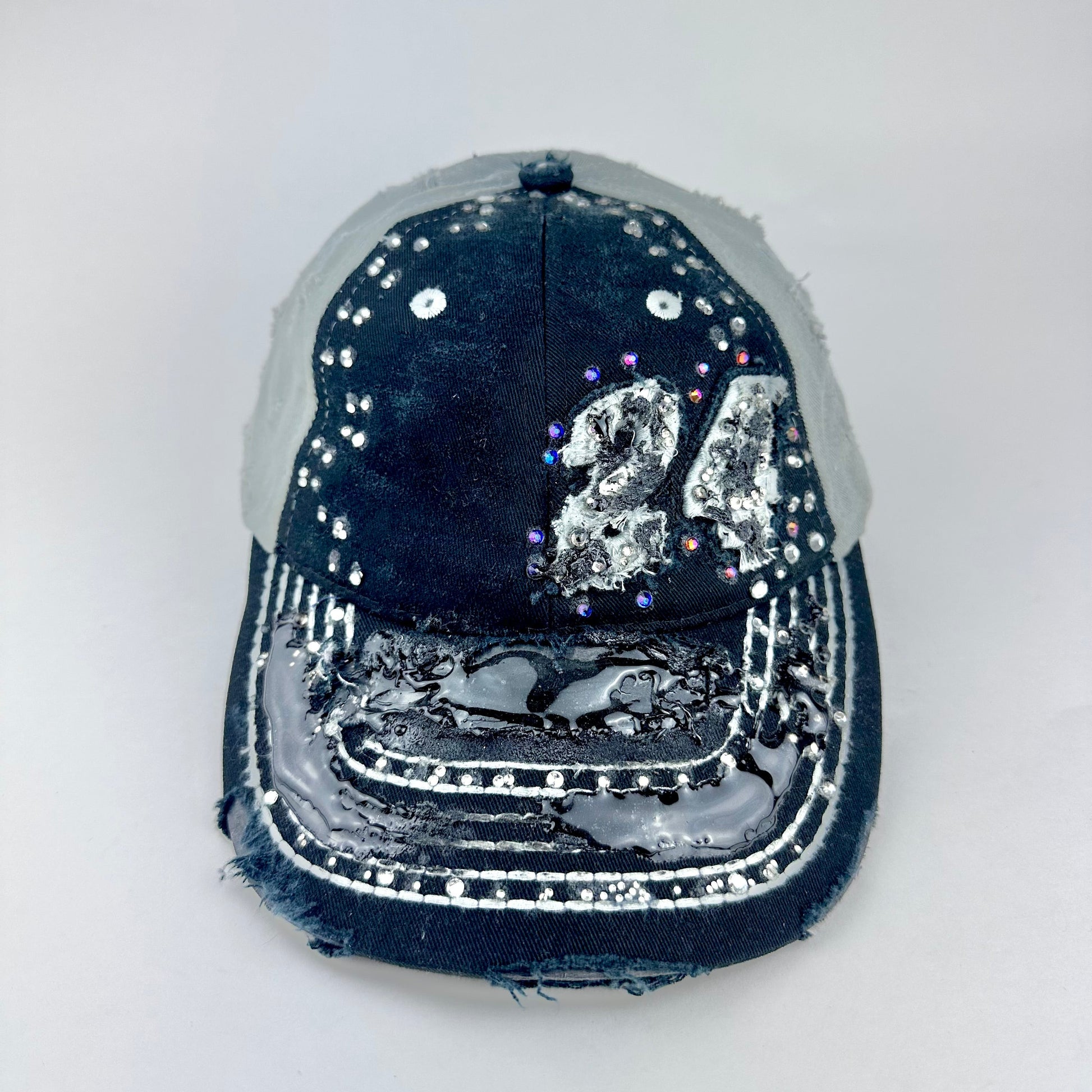 Front of ASTROBOI* “24” black racing cap with silver rhinestones, white stitching, glossy black resin details, and adjustable Velcro back closure.