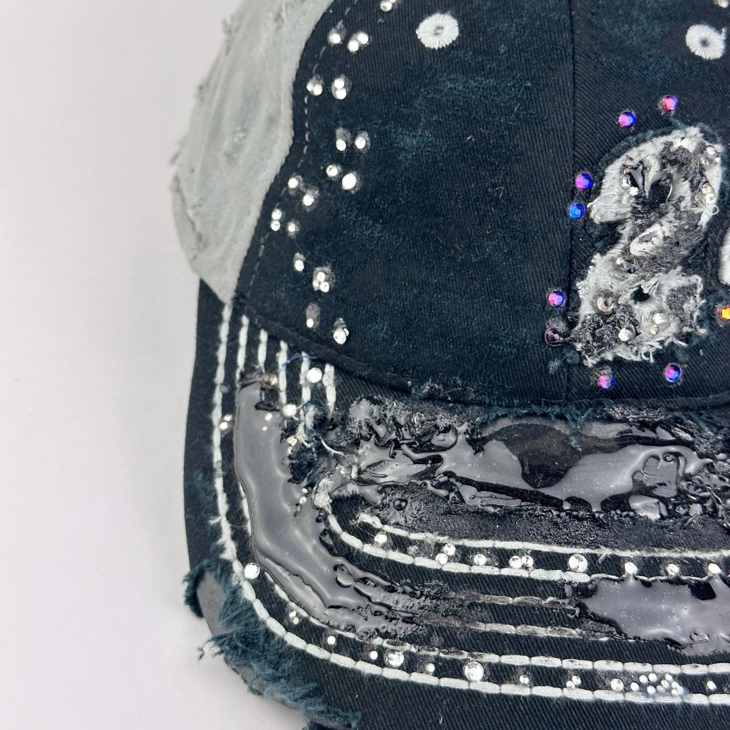 Left side detail of ASTROBOI* “24” black racing cap with silver rhinestones, white stitching, glossy black resin details, and adjustable Velcro back closure.
