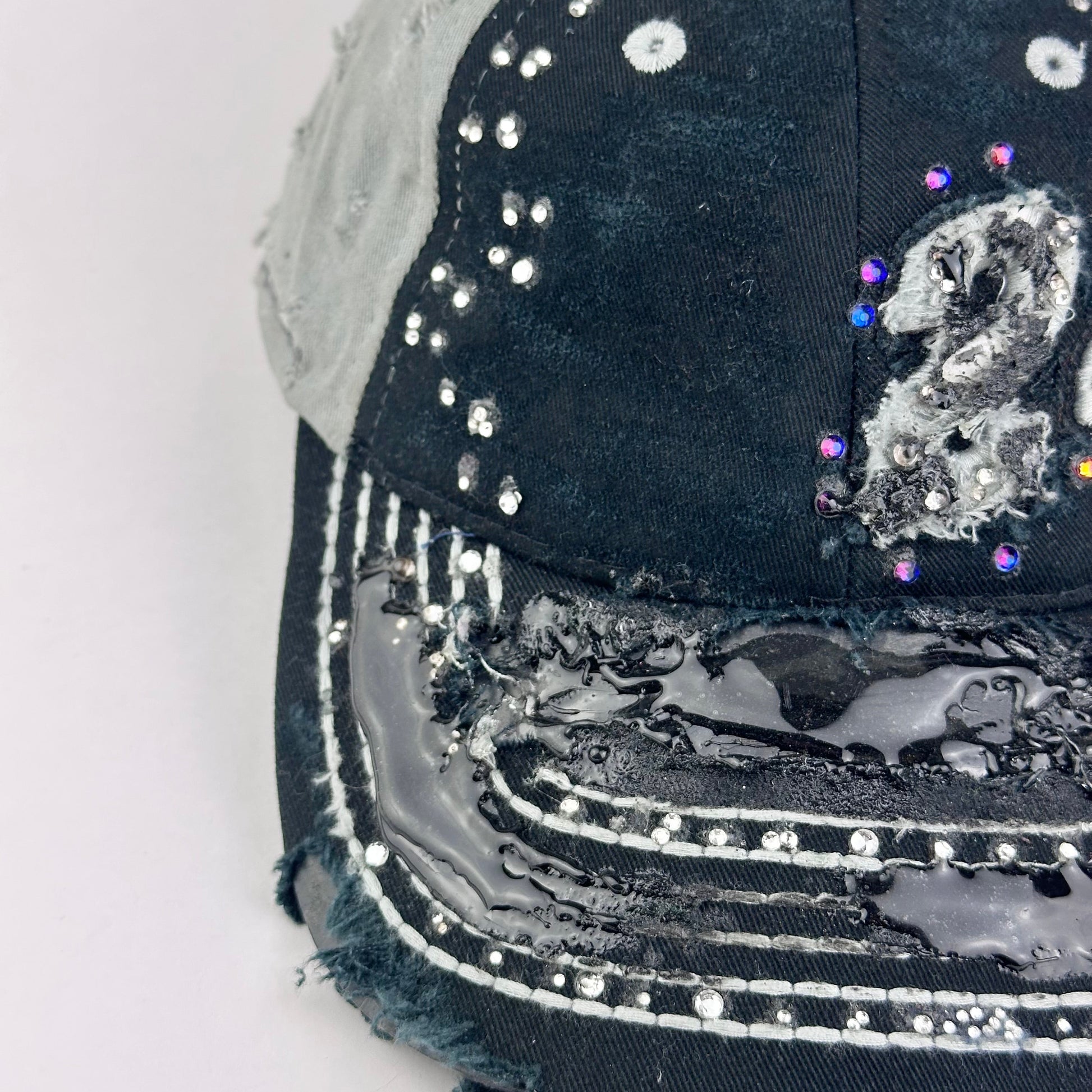 Left side detail of ASTROBOI* “24” black racing cap with silver rhinestones, white stitching, glossy black resin details, and adjustable Velcro back closure.