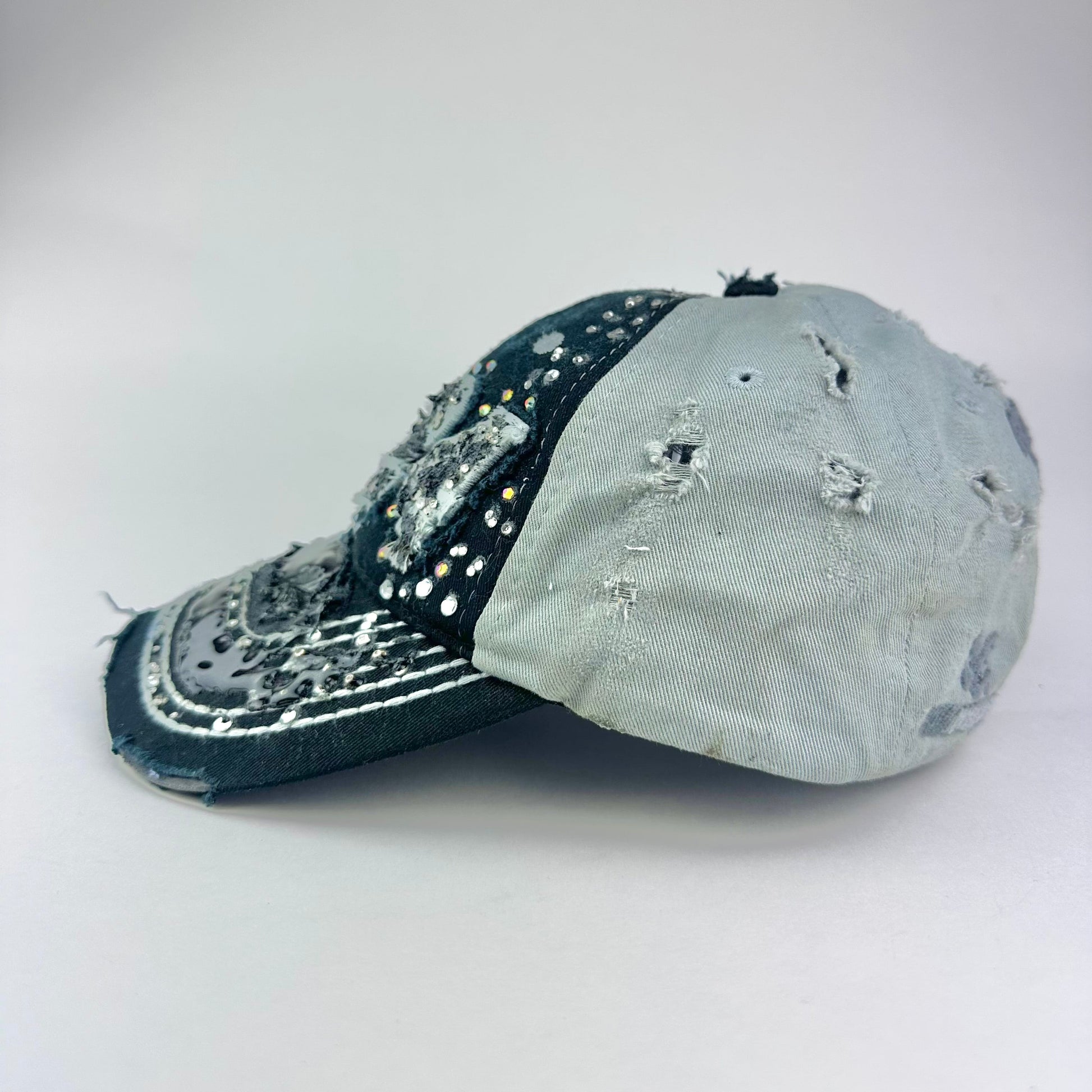 Left side of ASTROBOI* “24” black racing cap with silver rhinestones, white stitching, glossy black resin details, and adjustable Velcro back closure.