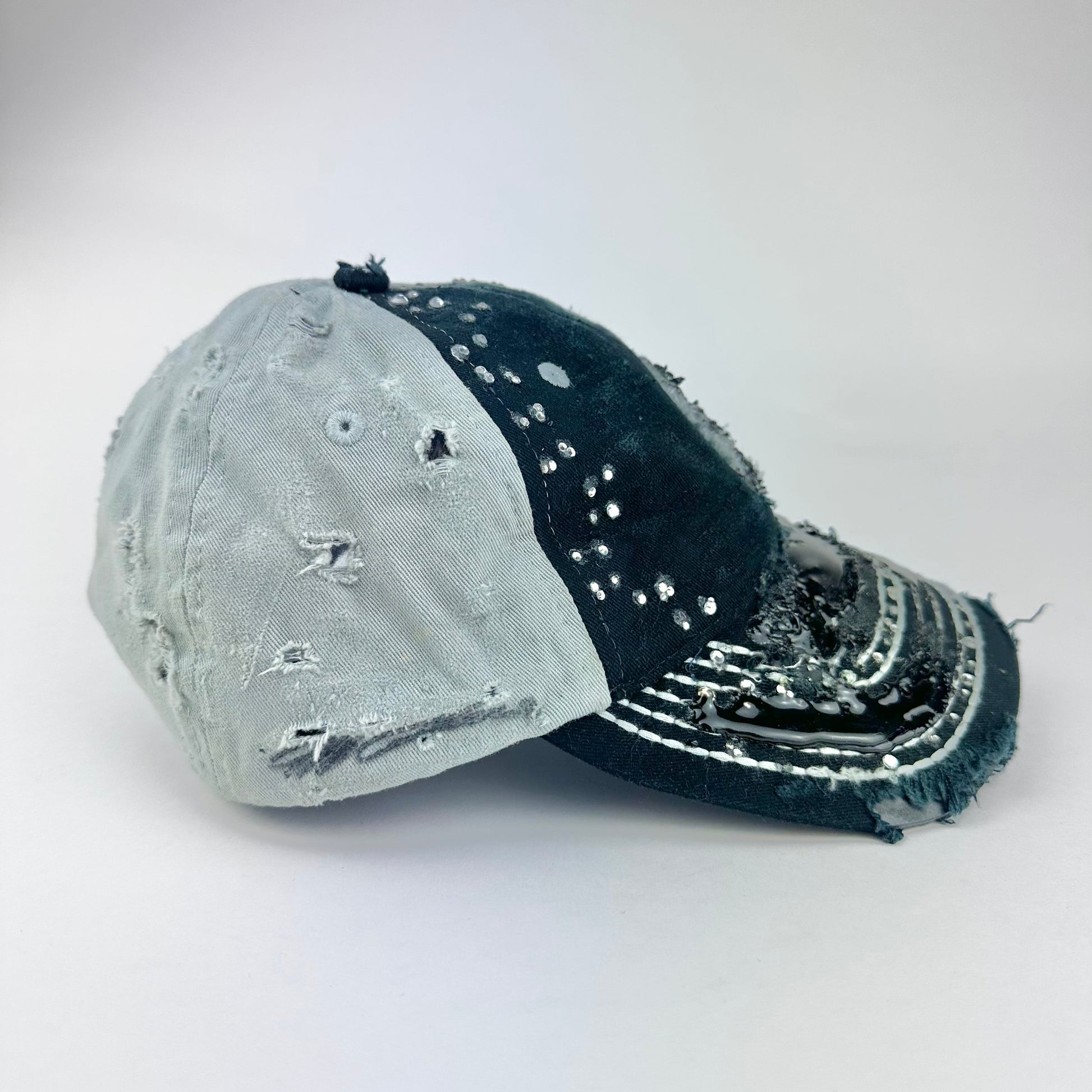 Right side of ASTROBOI* “24” black racing cap with silver rhinestones, white stitching, glossy black resin details, and adjustable Velcro back closure.