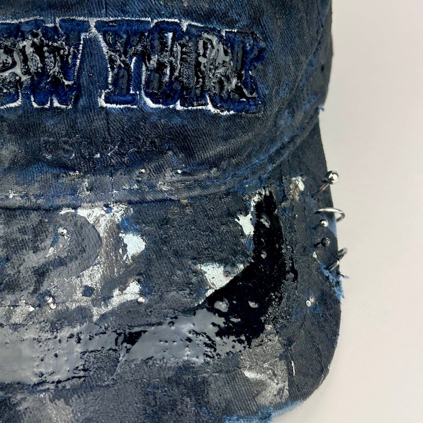 Front right visor detail on ASTROBOI* Zypher NYC navy distressed hat with metallic silver paint, black resin logo and brim, adjustable back streetwear cap.