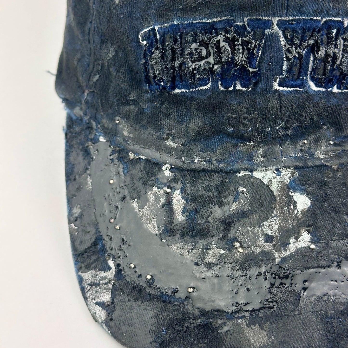 Front left detail on visor of ASTROBOI* Zypher NYC navy distressed hat with metallic silver paint, black resin logo and brim, adjustable back streetwear cap.