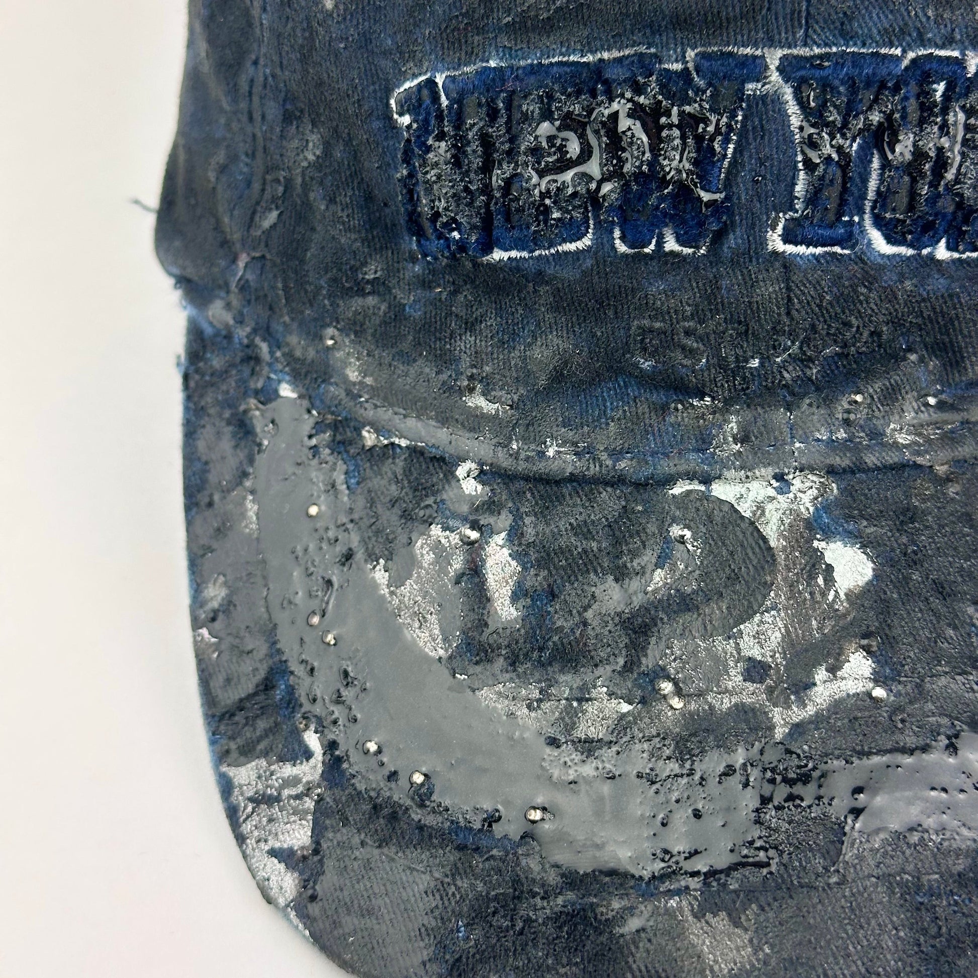 Front left detail on visor of ASTROBOI* Zypher NYC navy distressed hat with metallic silver paint, black resin logo and brim, adjustable back streetwear cap.