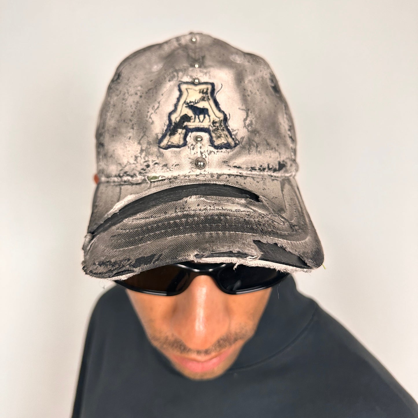 Front of Off-white and black faded ASTROBOI* x Abercrombie hat with custom paint treatment and stainless steel piercing, handmade in NYC.