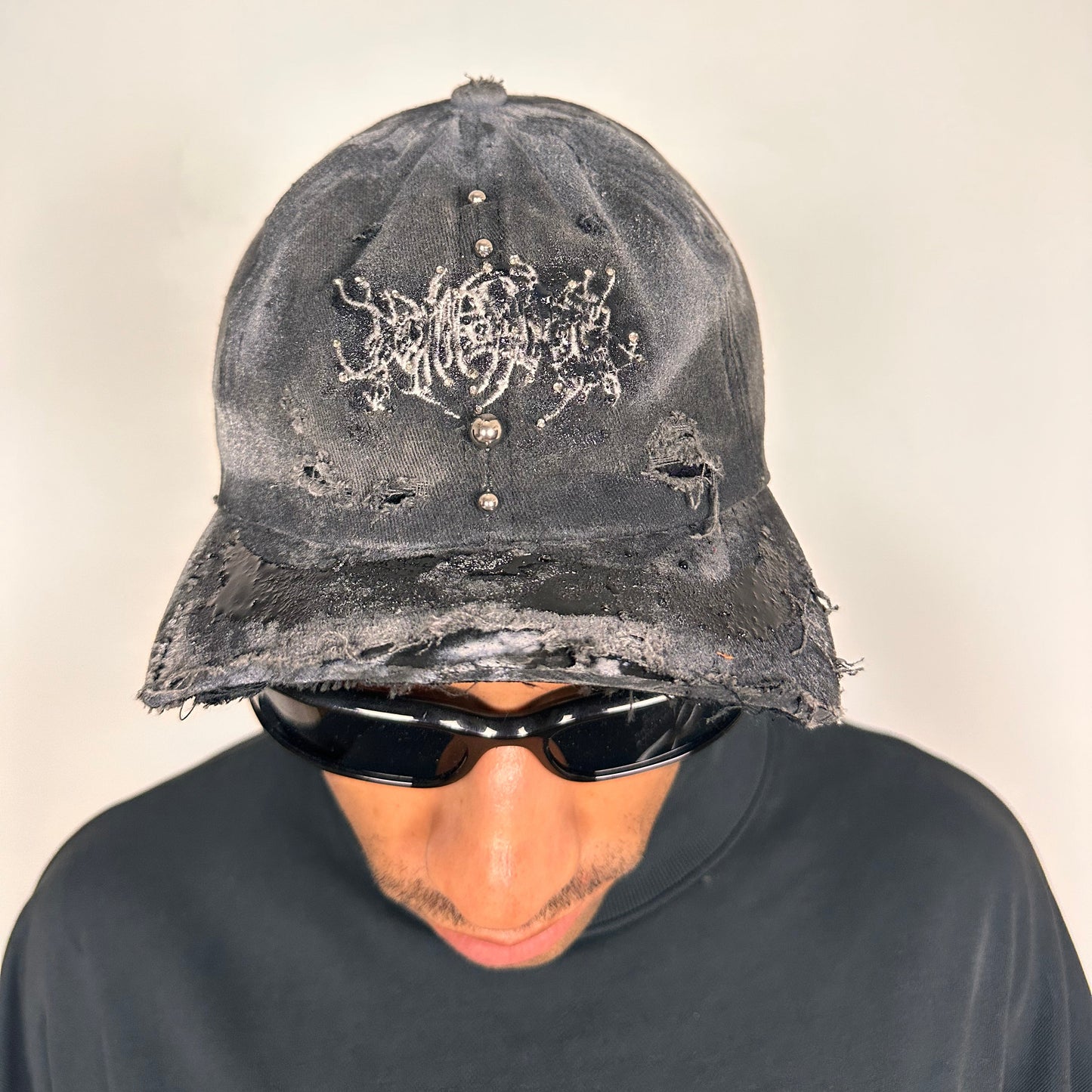 Front of ASTROBOI* Chalk black distressed half-visor hat with white airbrush detailing, rhinestones, resin accents, and stainless steel piercings.