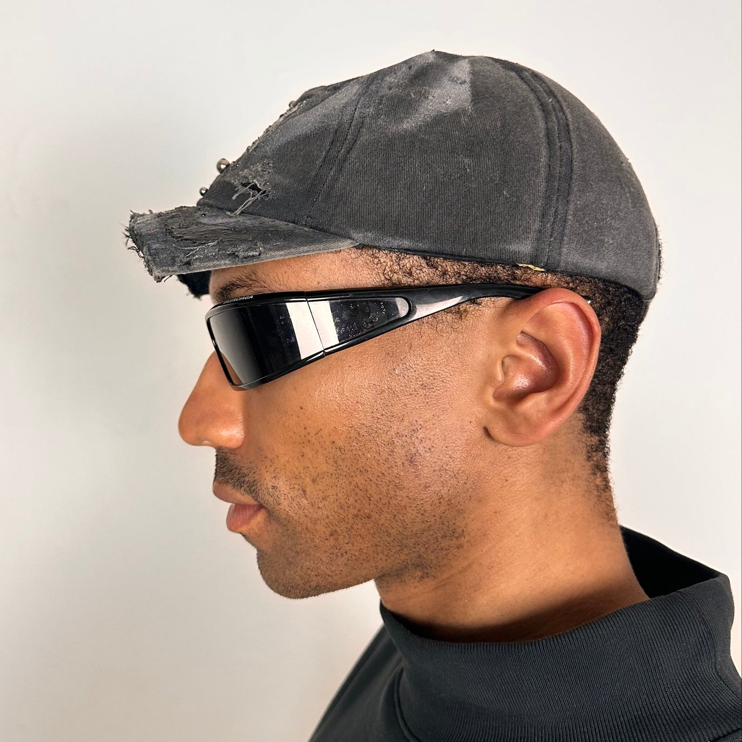 Left side of ASTROBOI* Chalk black distressed half-visor hat with white airbrush detailing, rhinestones, resin accents, and stainless steel piercings.