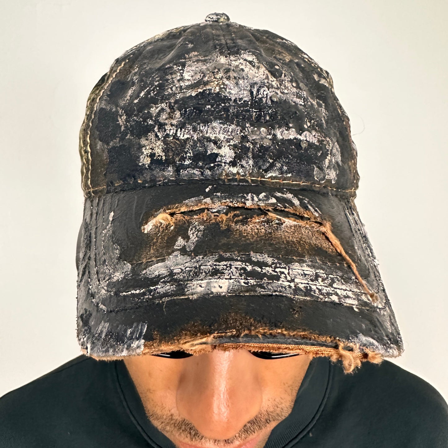 Front of ASTROBOI* x Mossy Oak brown RealTree camo hat with rhinestones, distressed paint details, and leather visor, adjustable fit.