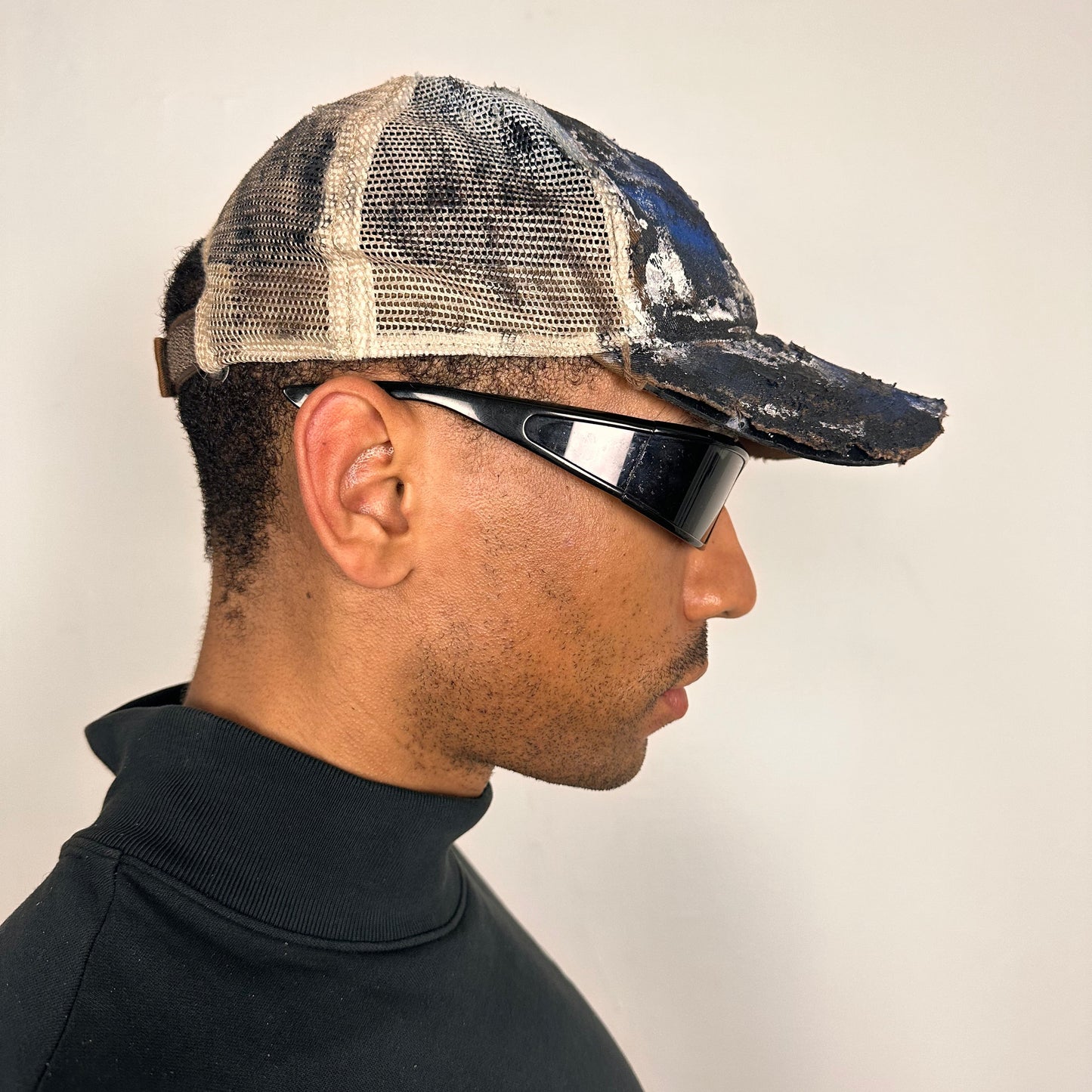 Right side of ASTROBOI* x John Deere black and blue distressed trucker hat with rhinestone resin logo and stainless steel piercings.