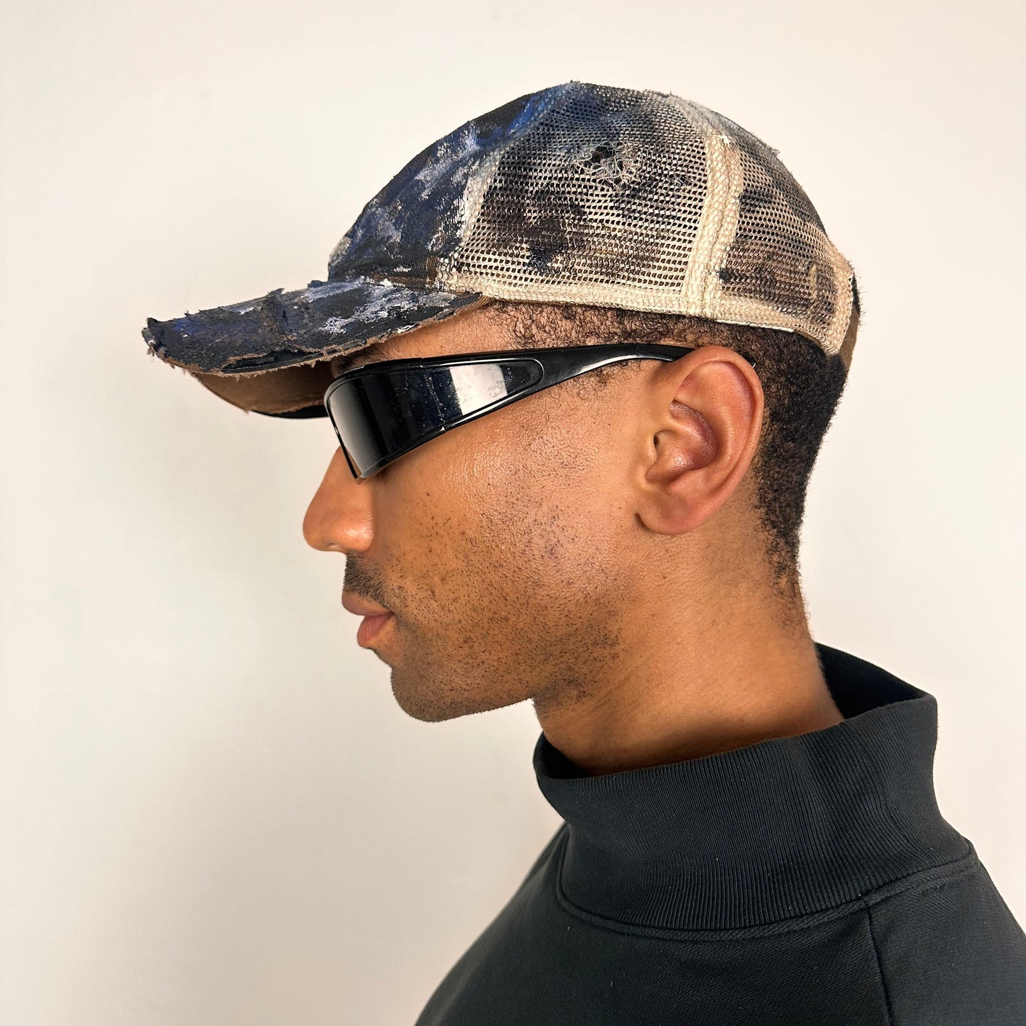 Left of ASTROBOI* x John Deere black and blue distressed trucker hat with rhinestone resin logo and stainless steel piercings.