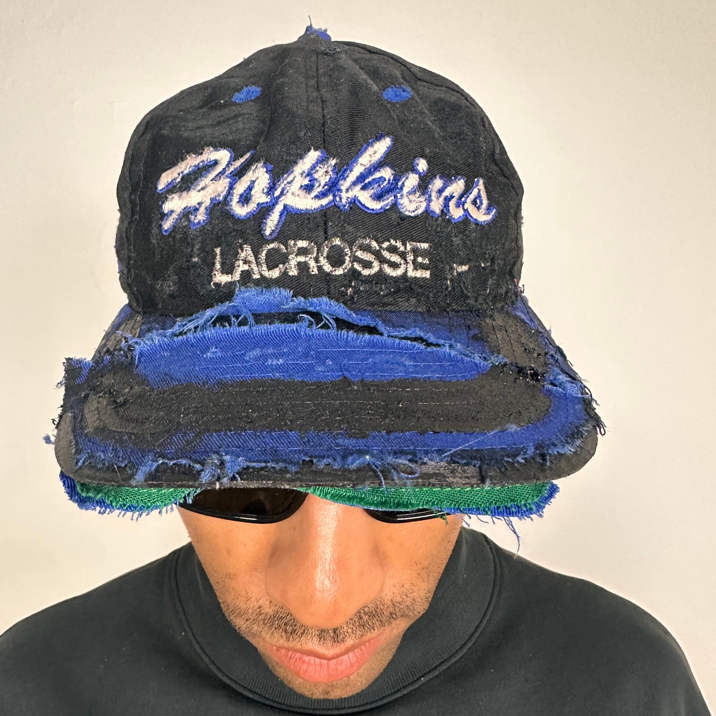 Front of Black distressed ASTROBOI* Hopkins Lacrosse cap with blue embroidery and custom black paint treatment, snapback style, handcrafted in NYC.