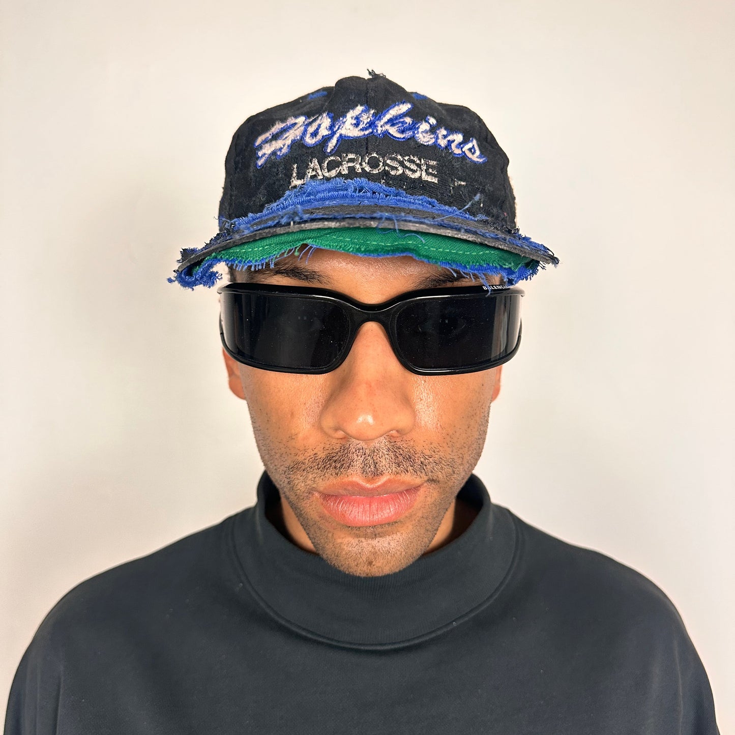 Overview of Black distressed ASTROBOI* Hopkins Lacrosse cap with blue embroidery and custom black paint treatment, snapback style, handcrafted in NYC.