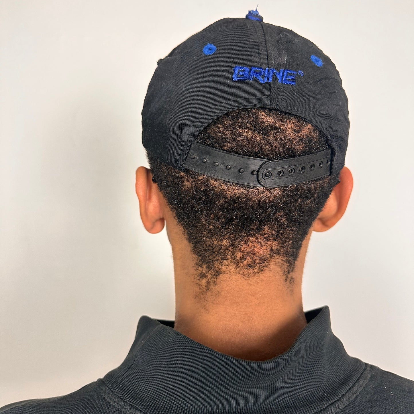Back of Black distressed ASTROBOI* Hopkins Lacrosse cap with blue embroidery and custom black paint treatment, snapback style, handcrafted in NYC.