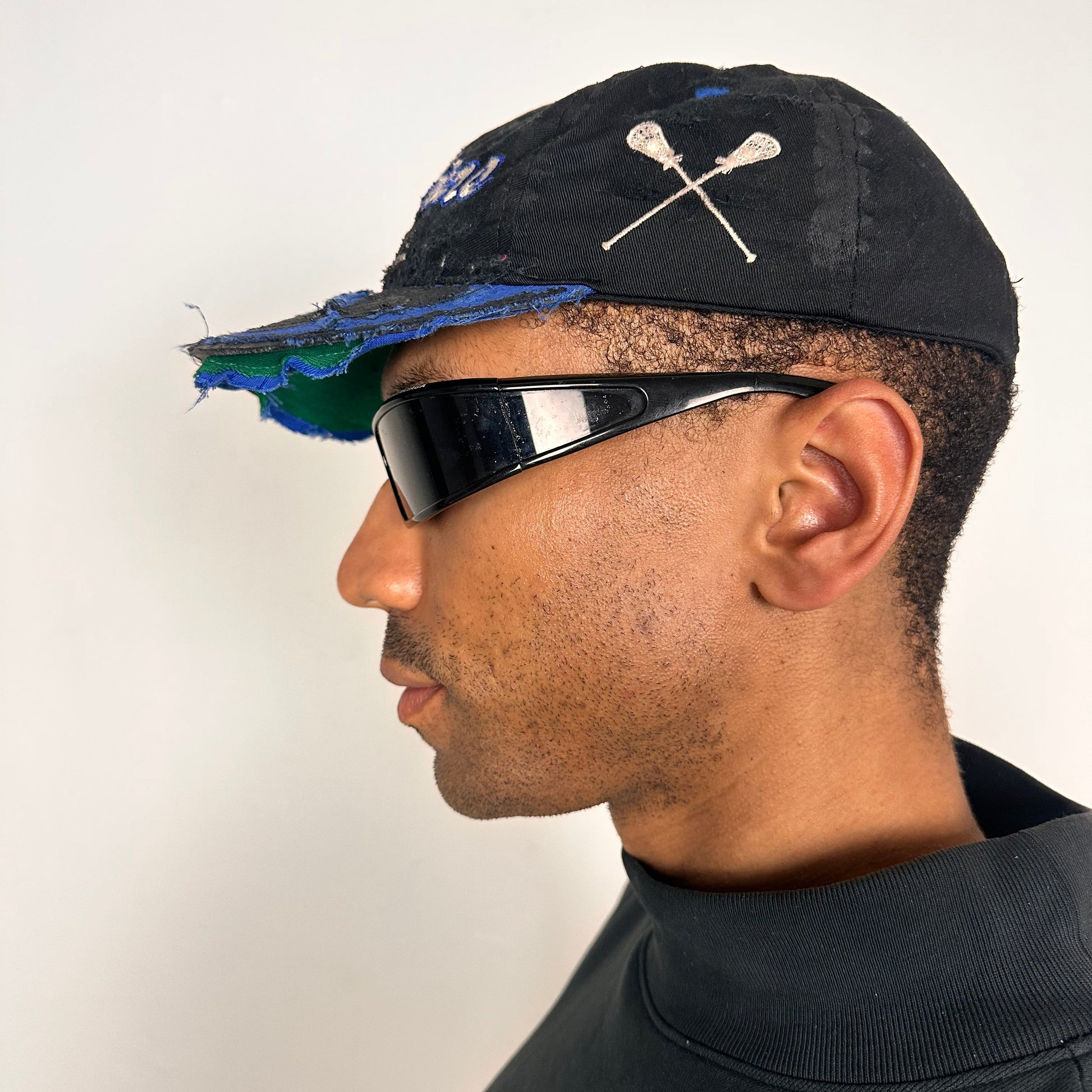 Left of Black distressed ASTROBOI* Hopkins Lacrosse cap with blue embroidery and custom black paint treatment, snapback style, handcrafted in NYC.