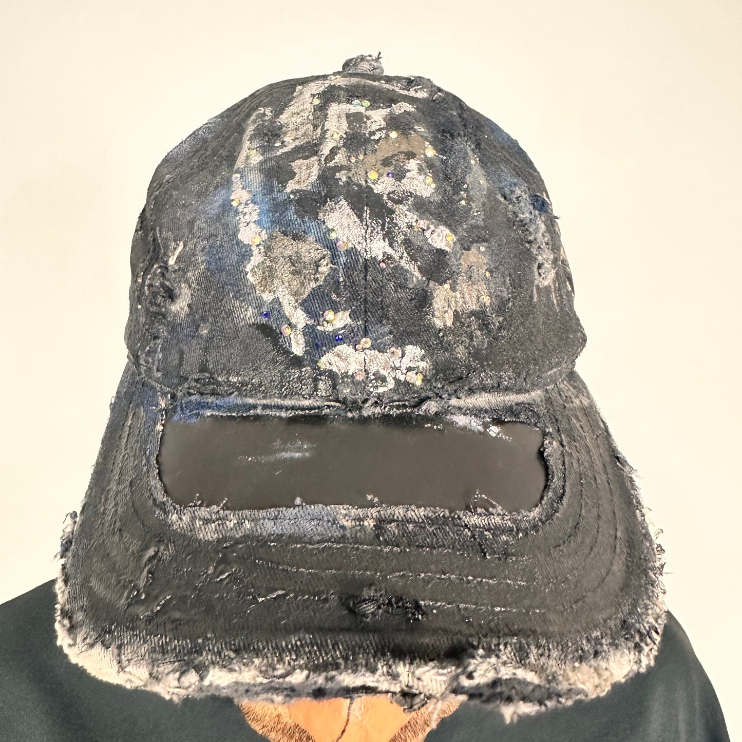 Front image of Black acid-washed denim hat with silver paint accents, multicolored rhinestones, and a ripped visor seam, customized by ASTROBOI* STUDIO.