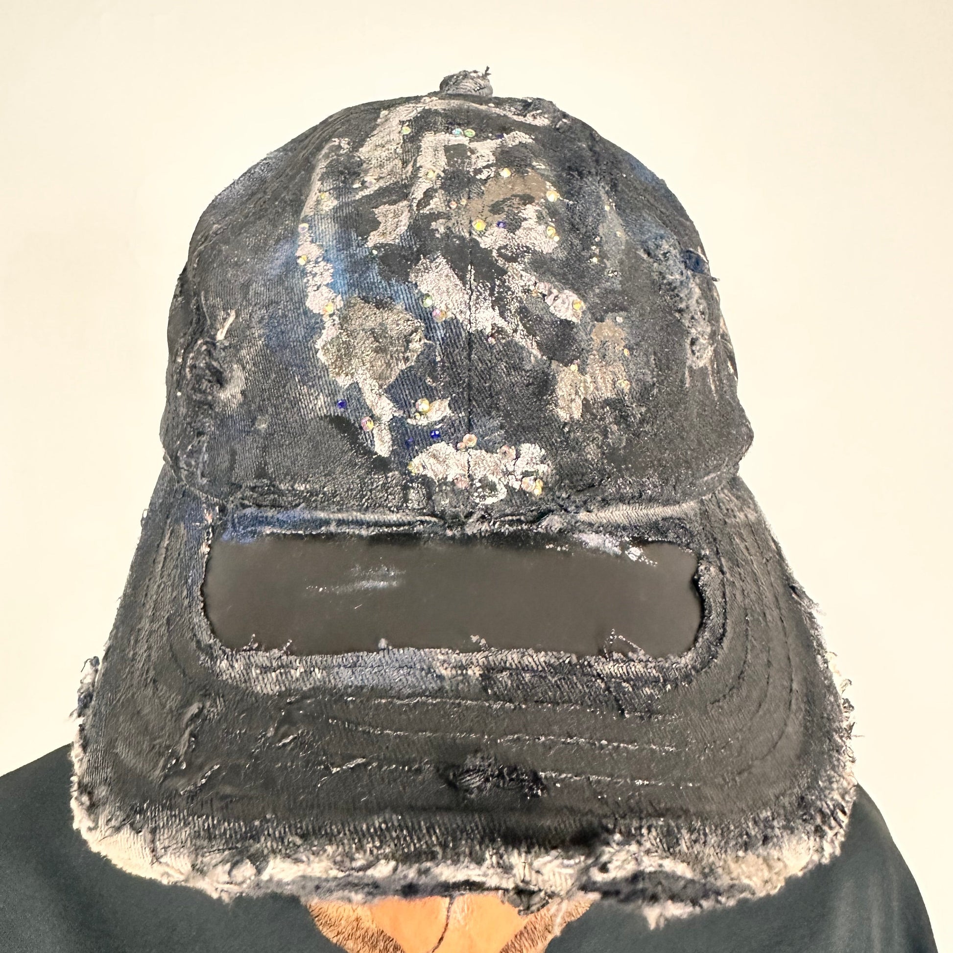 Front image of Black acid-washed denim hat with silver paint accents, multicolored rhinestones, and a ripped visor seam, customized by ASTROBOI* STUDIO.