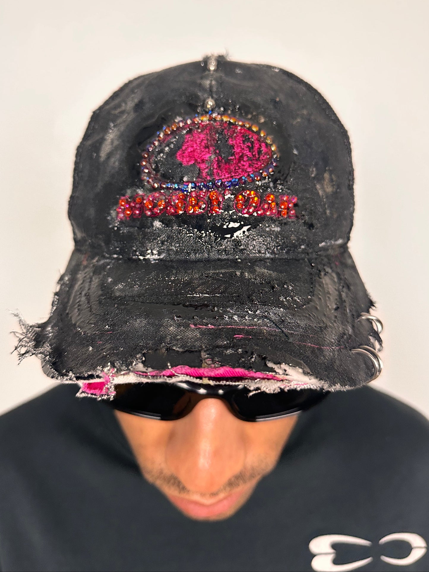 Front of ASTROBOI* x Mossy Oak black and pink distressed rhinestone hat with resin logo and mesh back panel