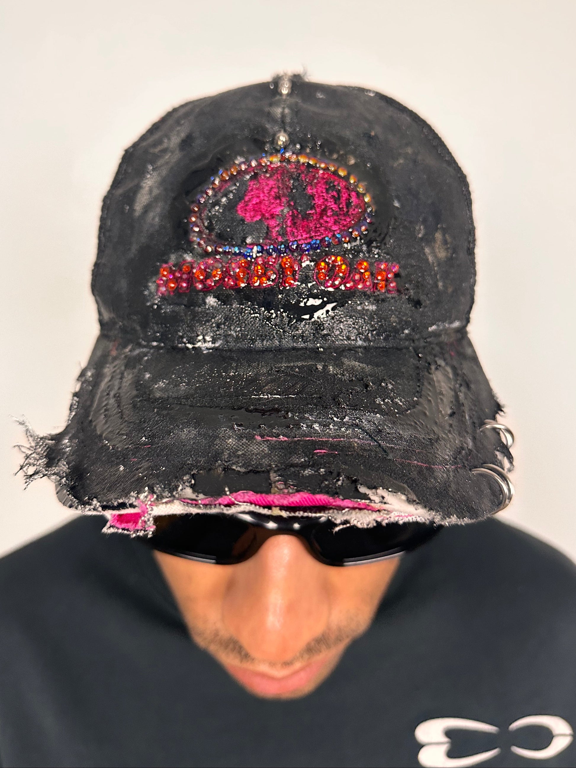 Front of ASTROBOI* x Mossy Oak black and pink distressed rhinestone hat with resin logo and mesh back panel