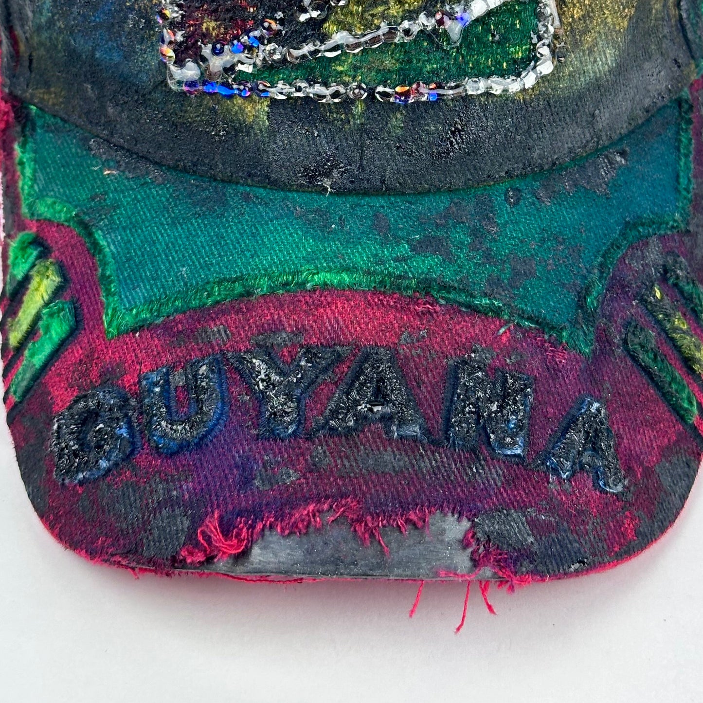 Guyana logo detail on ASTROBOI* Guyana yellow red green distressed baseball hat with resin-sealed rhinestone logo patch and adjustable strap, hand-customized in NYC