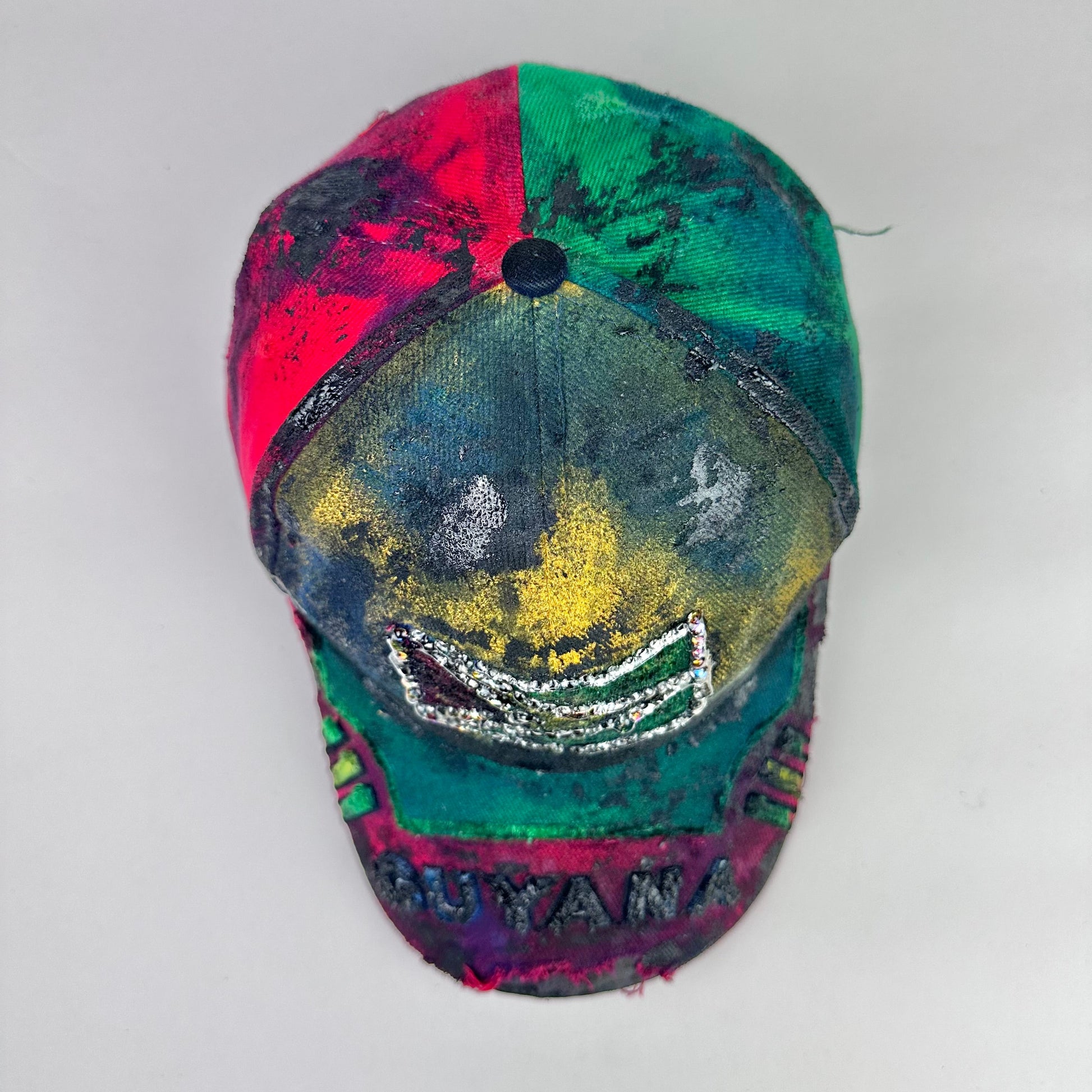 Top product shot of ASTROBOI* Guyana yellow red green distressed baseball hat with resin-sealed rhinestone logo patch and adjustable strap, hand-customized in NYC