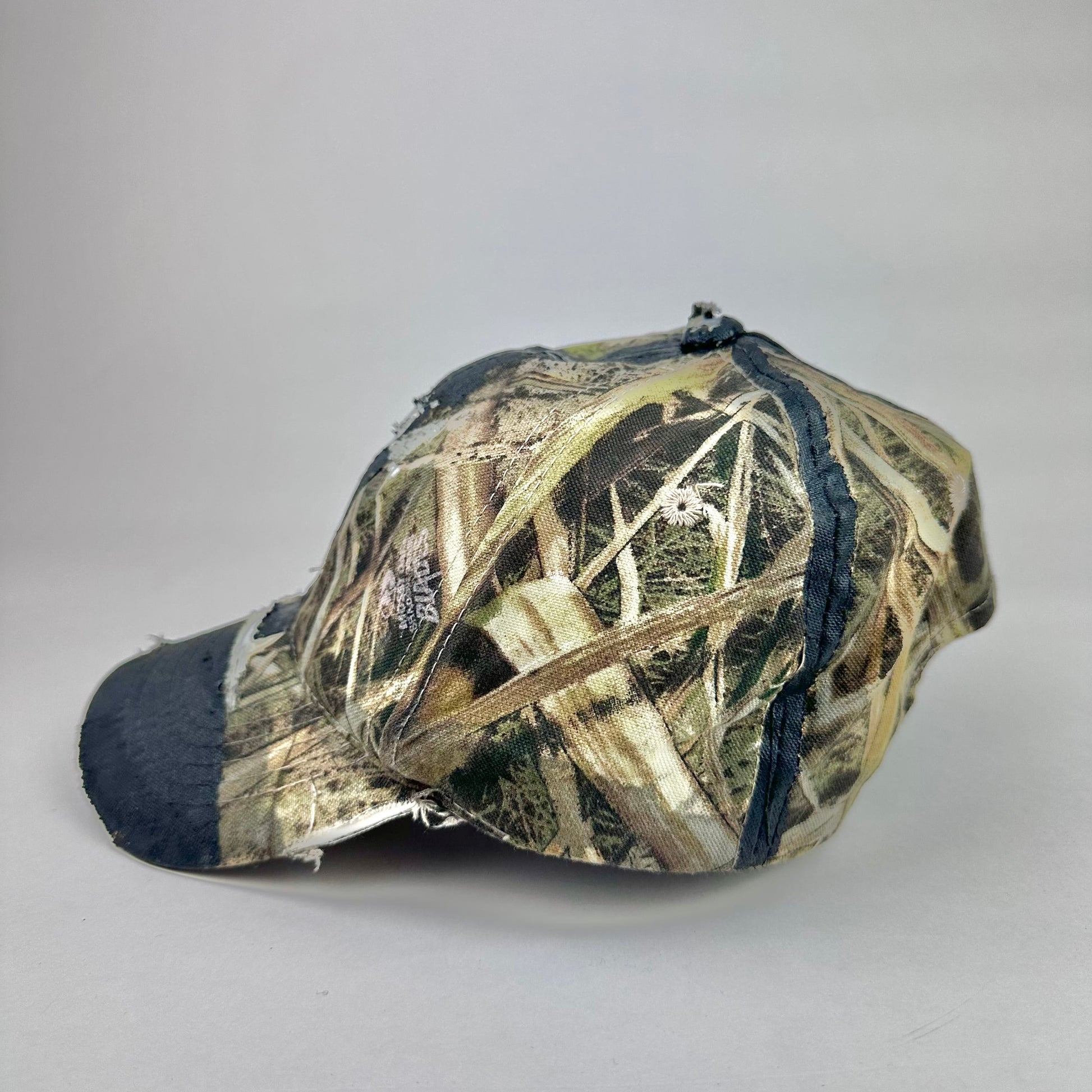 Left side of ASTROBOI* x Mossy Oak brown RealTree camouflage tattoo hat with SWA embroidery, black painted distressing, youth size, custom NYC piece