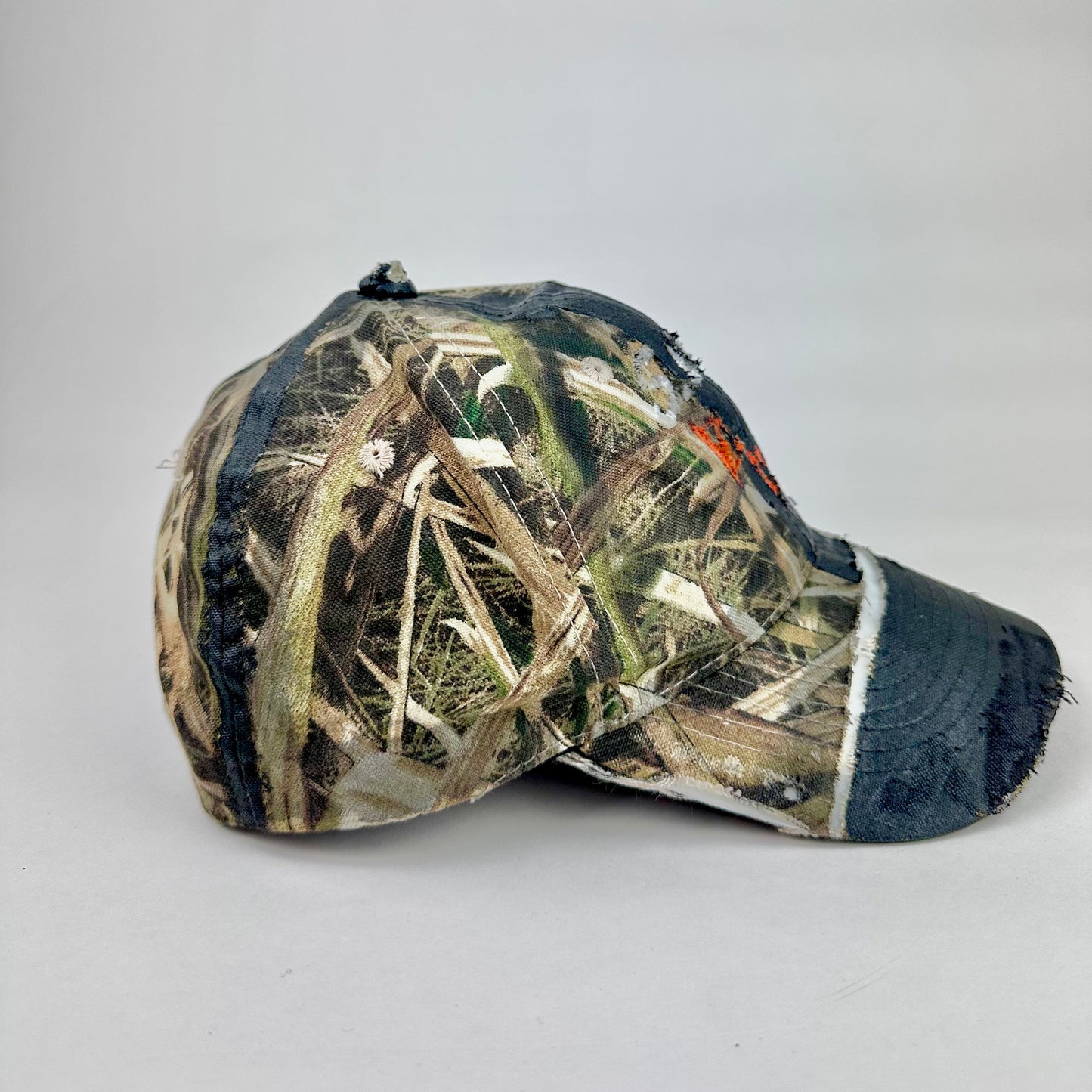 Right side of ASTROBOI* x Mossy Oak brown RealTree camouflage tattoo hat with SWA embroidery, black painted distressing, youth size, custom NYC piece