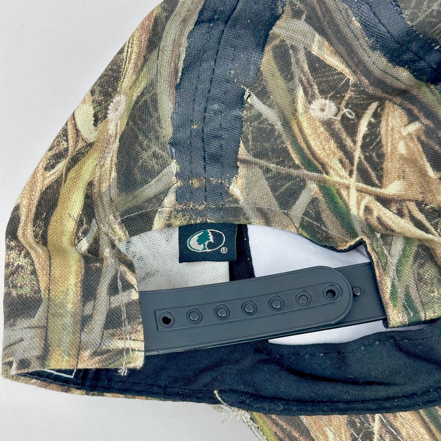 Back of ASTROBOI* x Mossy Oak brown RealTree camouflage tattoo hat with SWA embroidery, black painted distressing, youth size, custom NYC piece