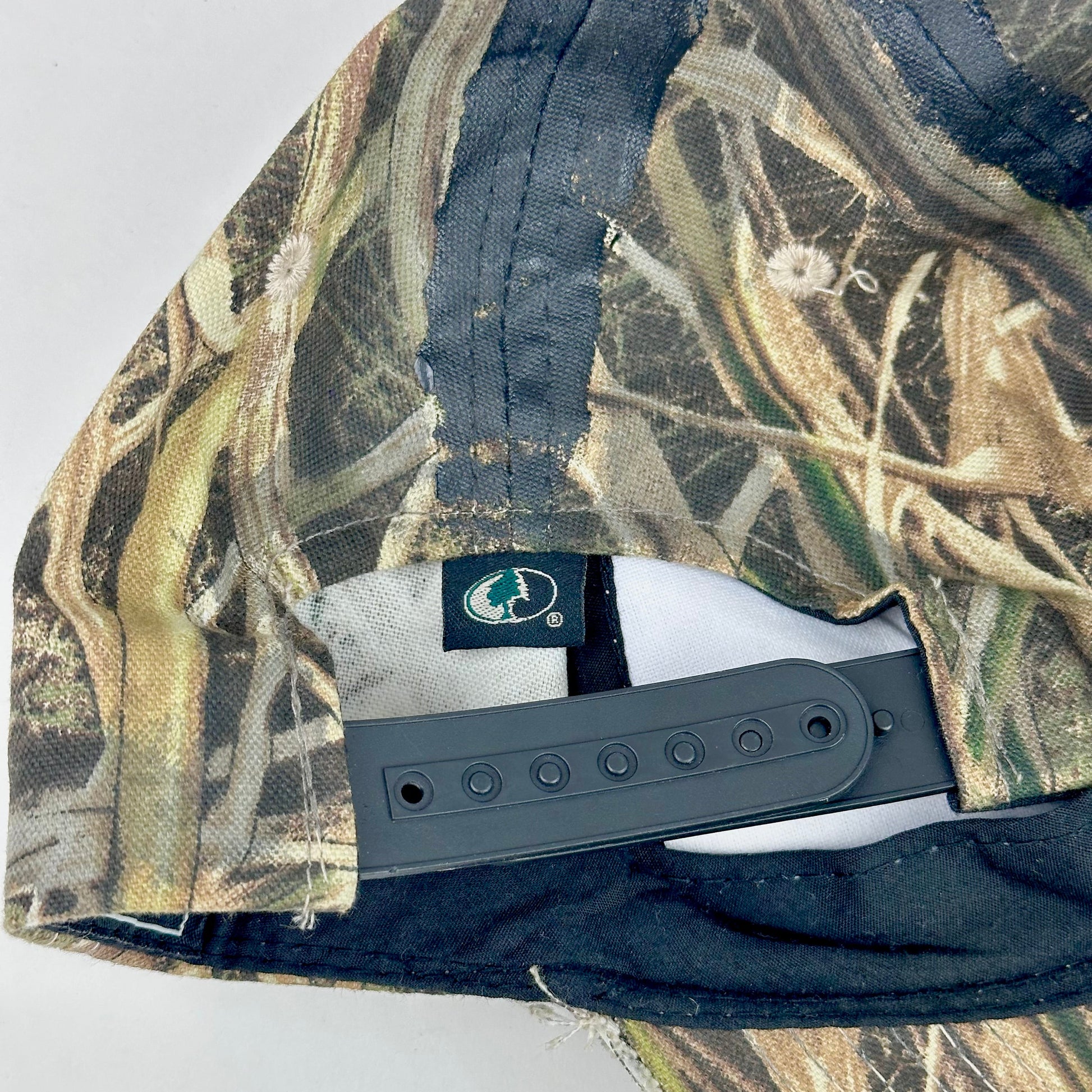 Back of ASTROBOI* x Mossy Oak brown RealTree camouflage tattoo hat with SWA embroidery, black painted distressing, youth size, custom NYC piece