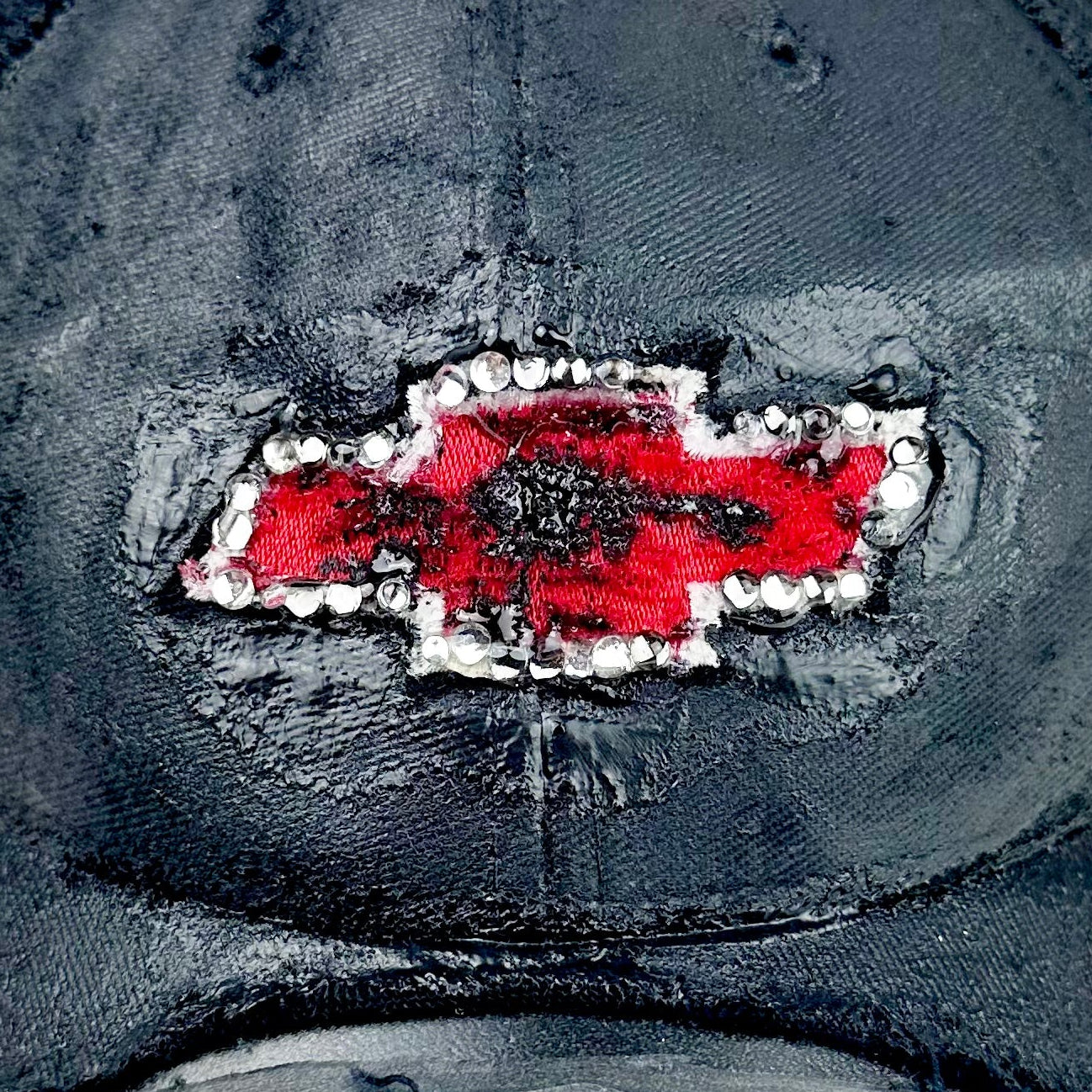 Close up of logo on ASTROBOI* x Chevy black distressed baseball hat with resin-sealed rhinestone logo, deconstructed visor, wax-painted tattoo details, adjustable fit
