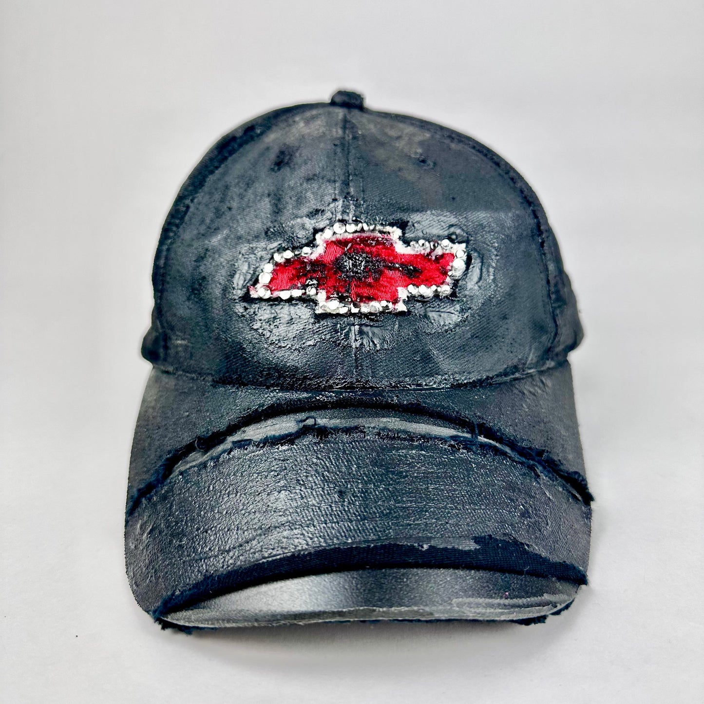 Still life front of ASTROBOI* x Chevy black distressed baseball hat with resin-sealed rhinestone logo, deconstructed visor, wax-painted tattoo details, adjustable fit