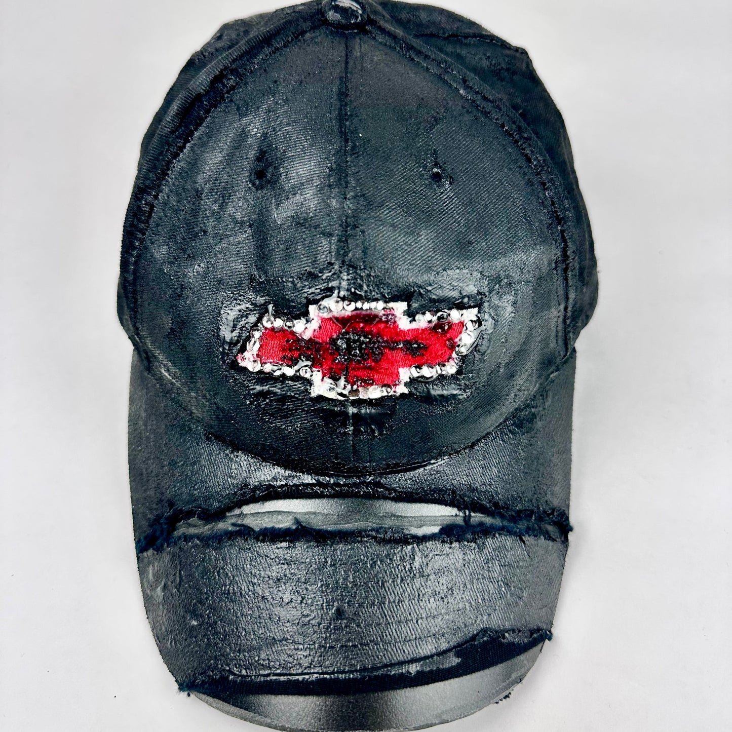 Still life front of ASTROBOI* x Chevy black distressed baseball hat with resin-sealed rhinestone logo, deconstructed visor, wax-painted tattoo details, adjustable fit
