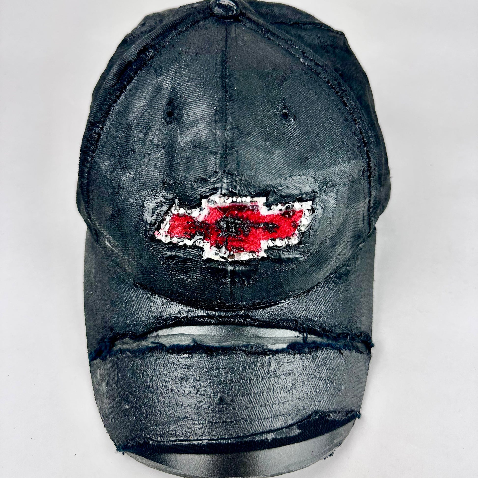 Still life front of ASTROBOI* x Chevy black distressed baseball hat with resin-sealed rhinestone logo, deconstructed visor, wax-painted tattoo details, adjustable fit