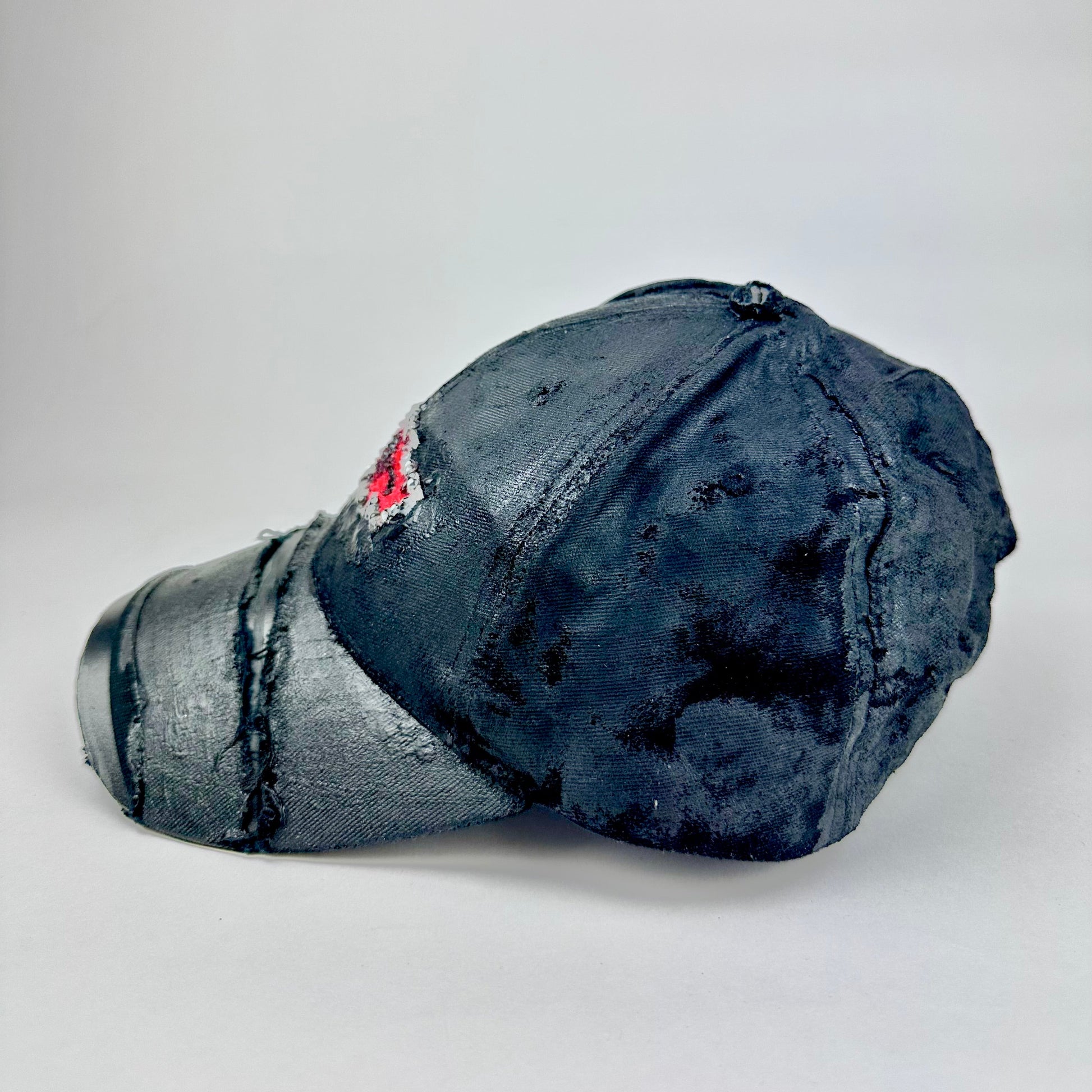 Flat lay left side of ASTROBOI* x Chevy black distressed baseball hat with resin-sealed rhinestone logo, deconstructed visor, wax-painted tattoo details, adjustable fit