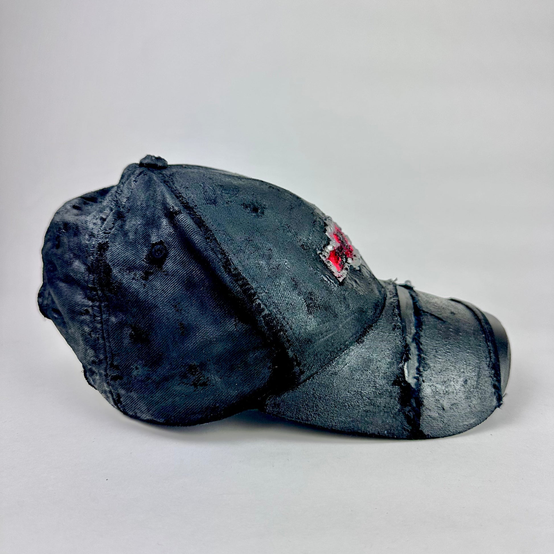 Flay lay left side of ASTROBOI* x Chevy black distressed baseball hat with resin-sealed rhinestone logo, deconstructed visor, wax-painted tattoo details, adjustable fit