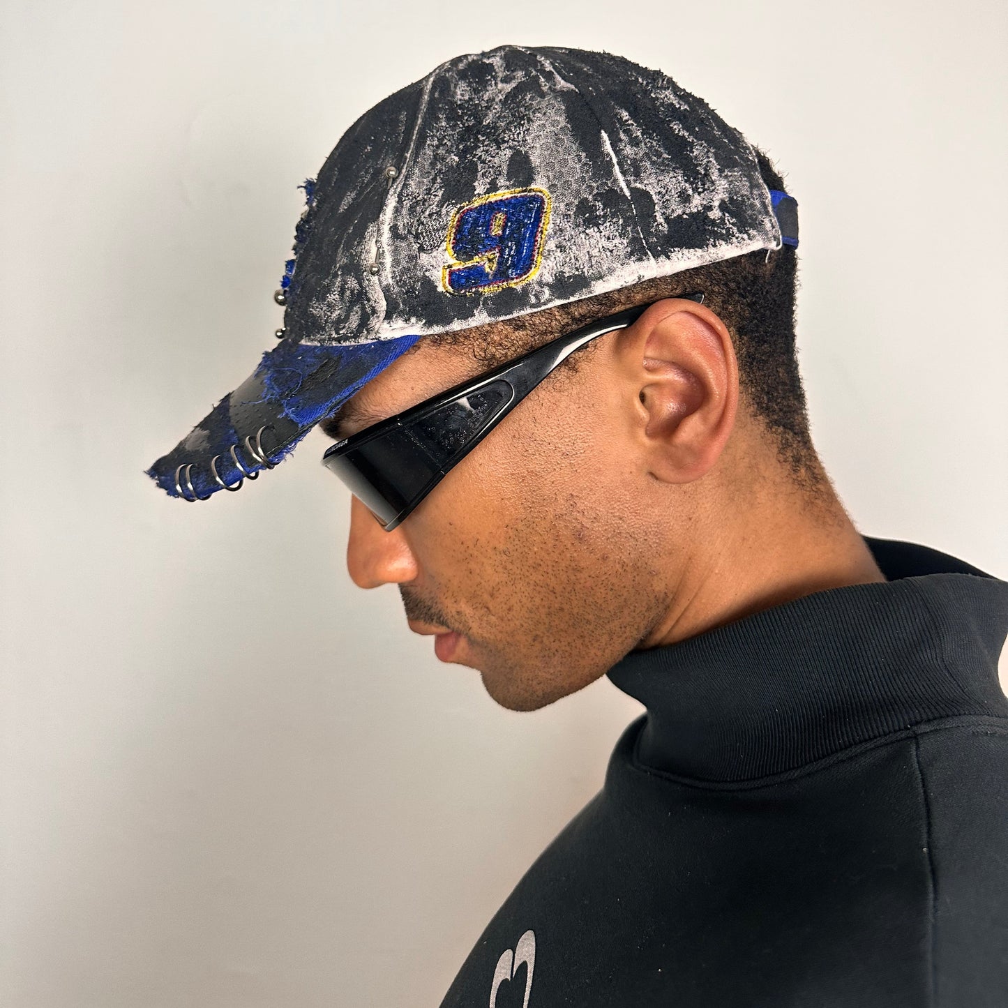 Left side of Blue and white ASTROBOI* NAPA hat with rhinestone-covered logo sealed in clear resin, stainless steel piercings, and a deconstructed visor, handcrafted in NYC.