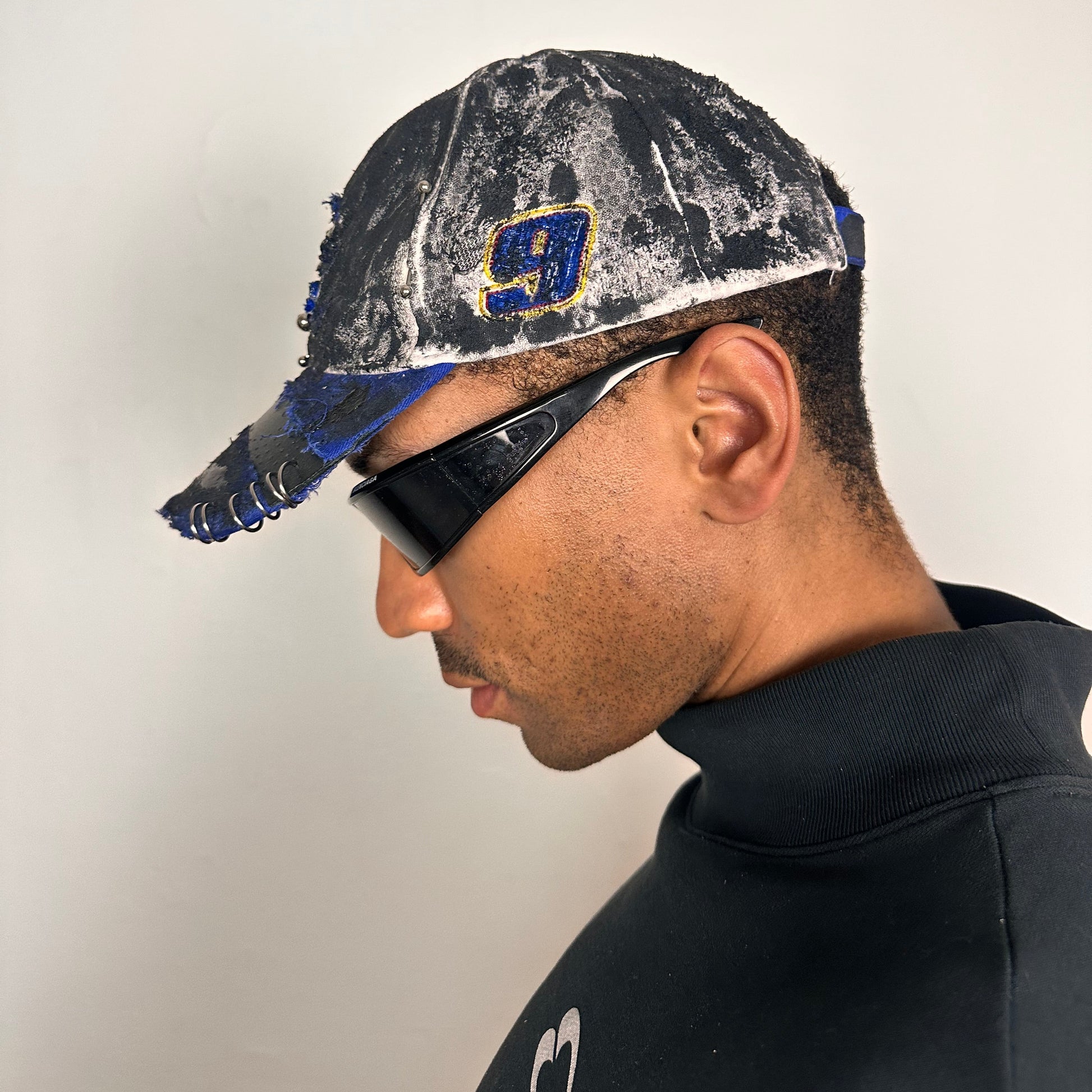 Left side of Blue and white ASTROBOI* NAPA hat with rhinestone-covered logo sealed in clear resin, stainless steel piercings, and a deconstructed visor, handcrafted in NYC.