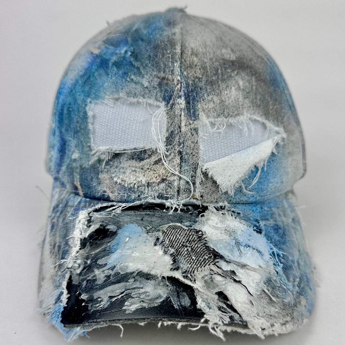 Front of ASTROBOI* Margiela blue deconstructed hat with distressed tears, airbrushed paint, denim scraps, silver staples and resin-coated visor.