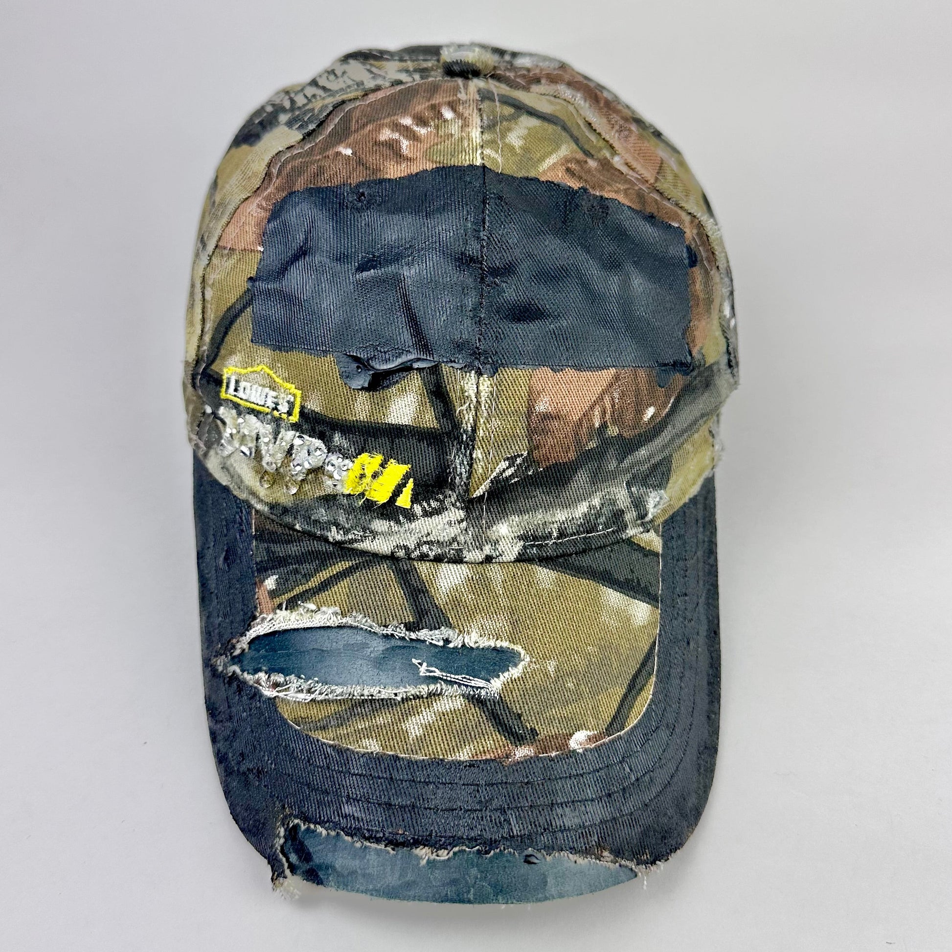 Still life front of ASTROBOI* x Lowe’s MVP brown RealTree camouflage hat with resin-sealed rhinestone logo, black waxed tattoo print, adjustable strap, custom NYC piece