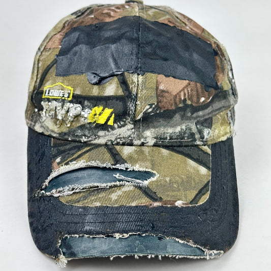 Still life close up of ASTROBOI* x Lowe’s MVP brown RealTree camouflage hat with resin-sealed rhinestone logo, black waxed tattoo print, adjustable strap, custom NYC piece